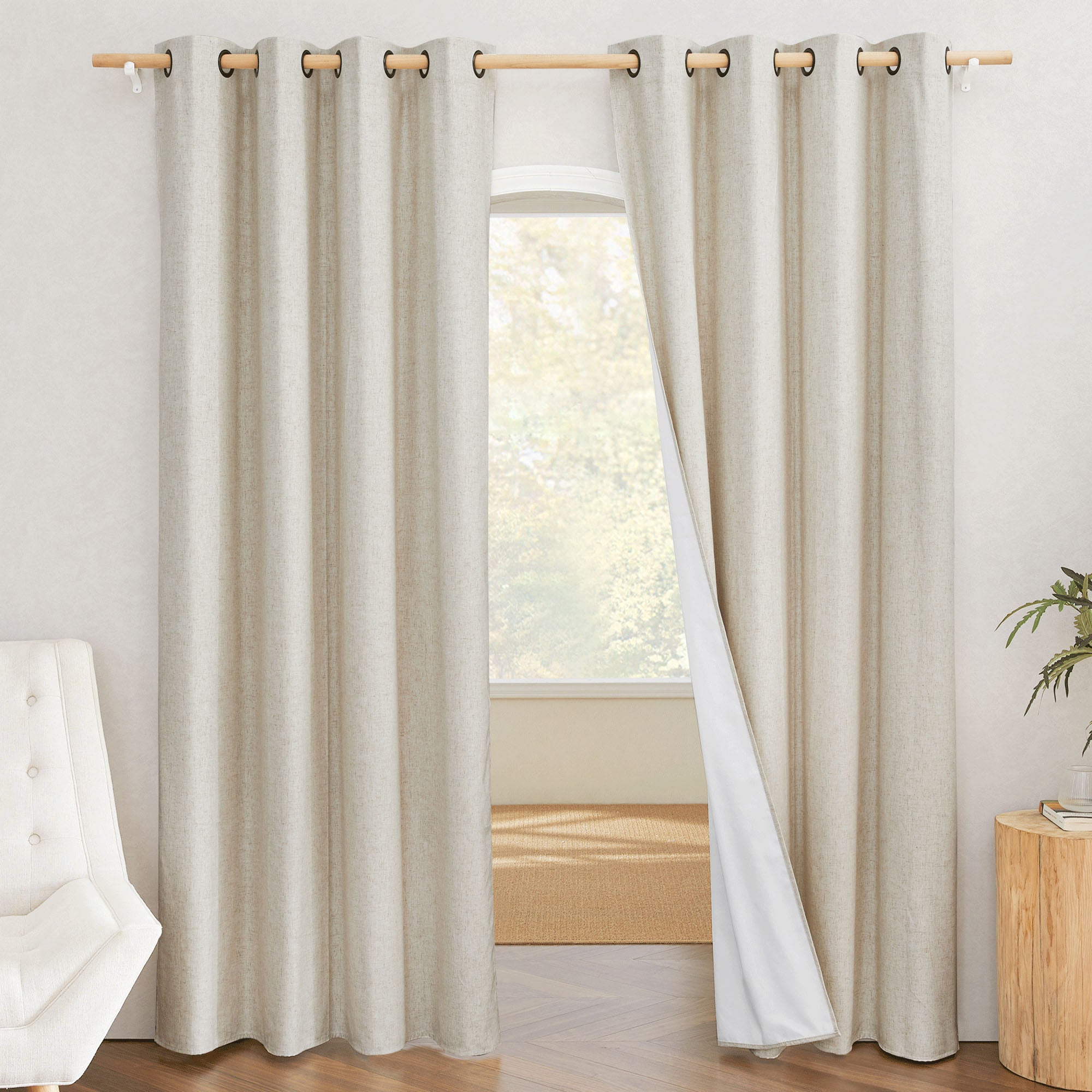 A pair of natural linen blackout curtains with grommets on a rod. One panel is pulled back to show the 100% white blackout liner.
