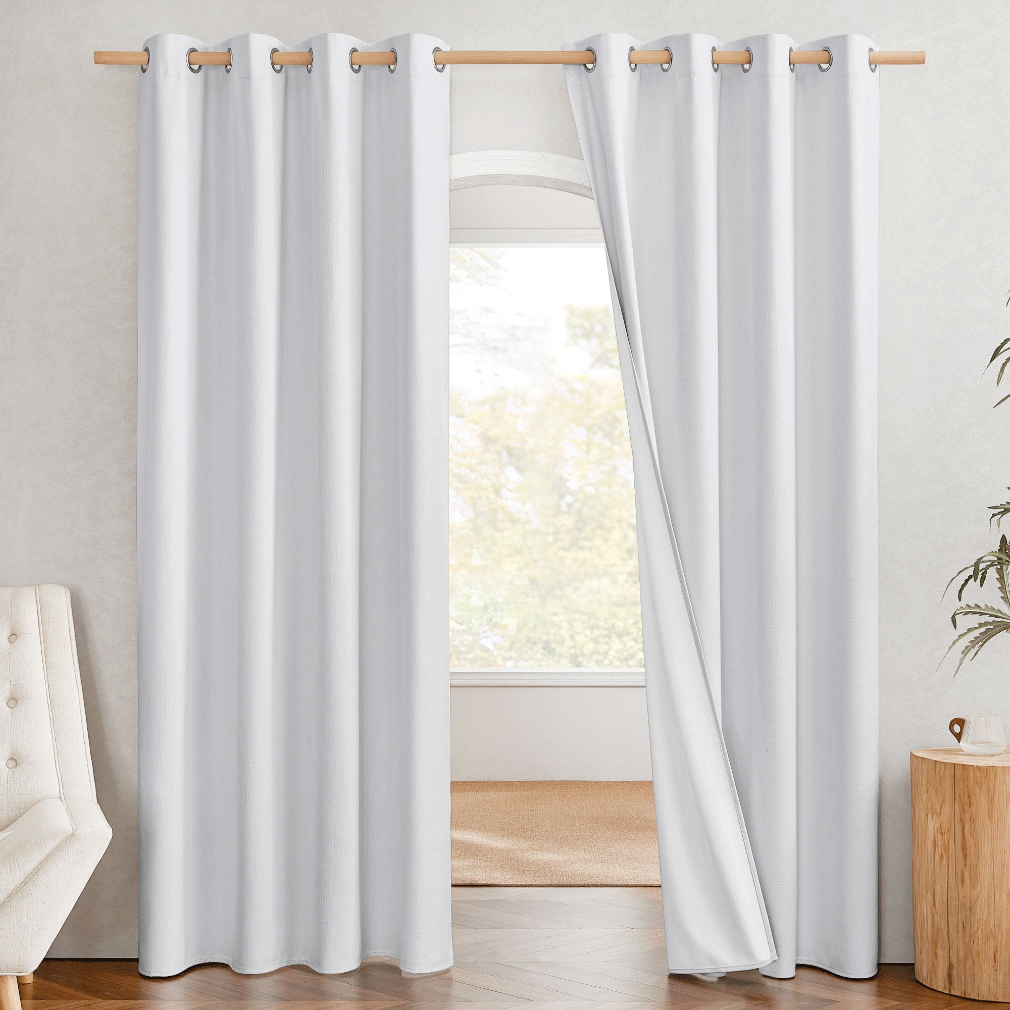 White blackout linen curtains with silver grommets on a rod. One panel is pulled back to show the 100% blackout lining.
