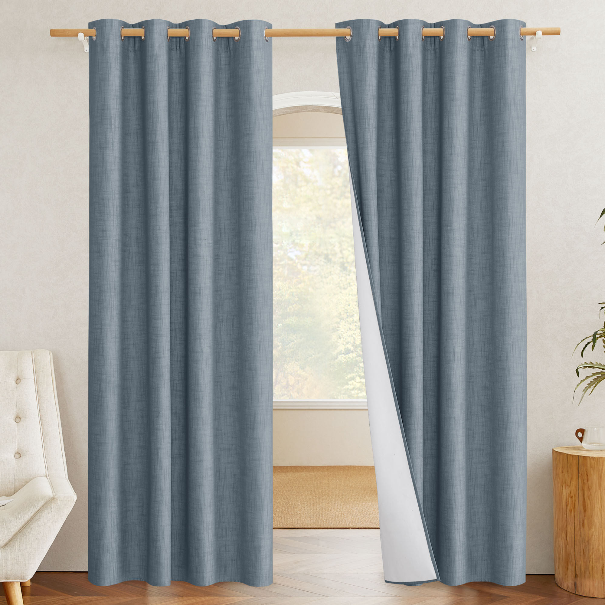 Blue linen blackout curtains hung on a grommet rod, with one panel pulled back to reveal the white blackout liner.