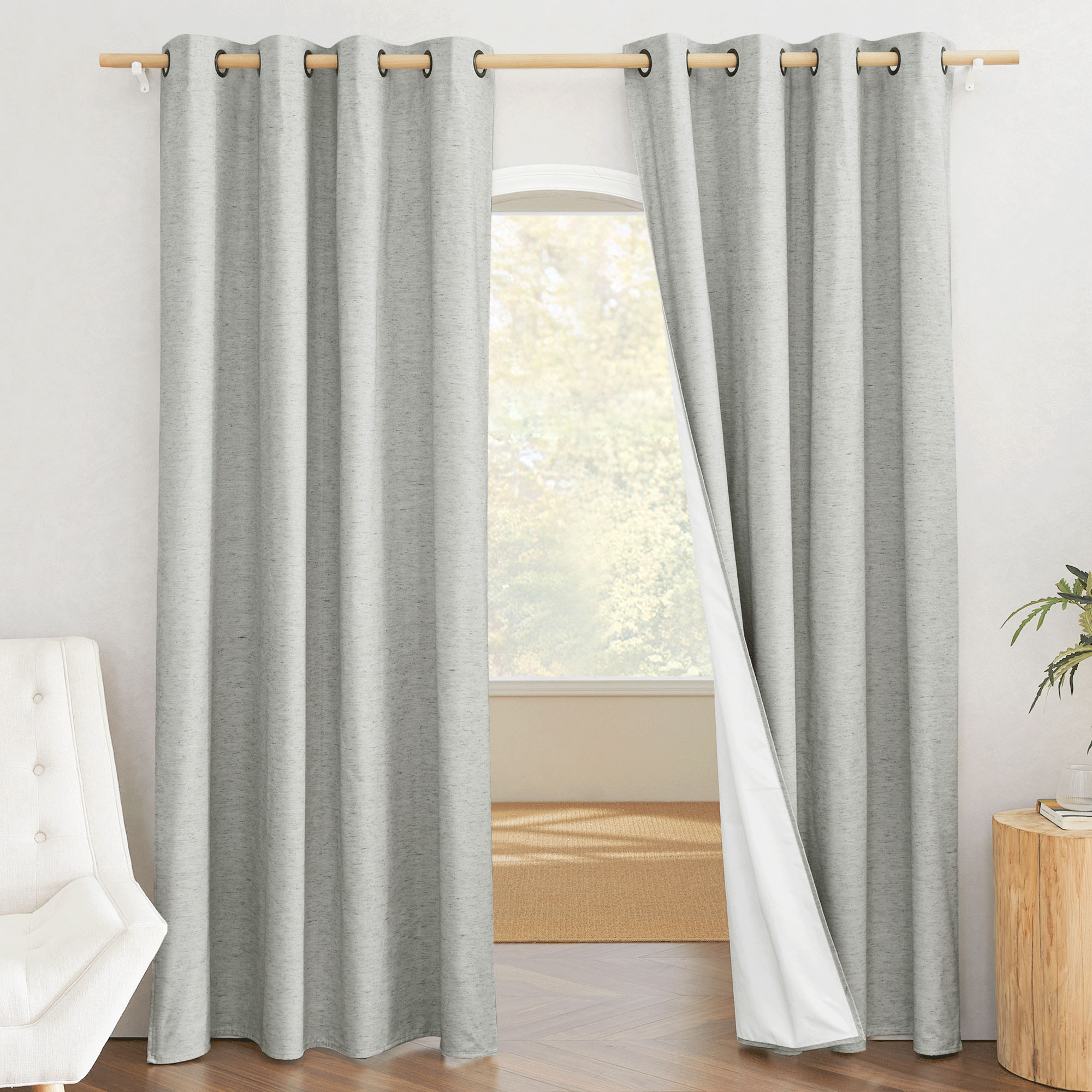 Grey grommet-top linen curtains in a room, with one panel pulled back to reveal the white 100% blackout lining.