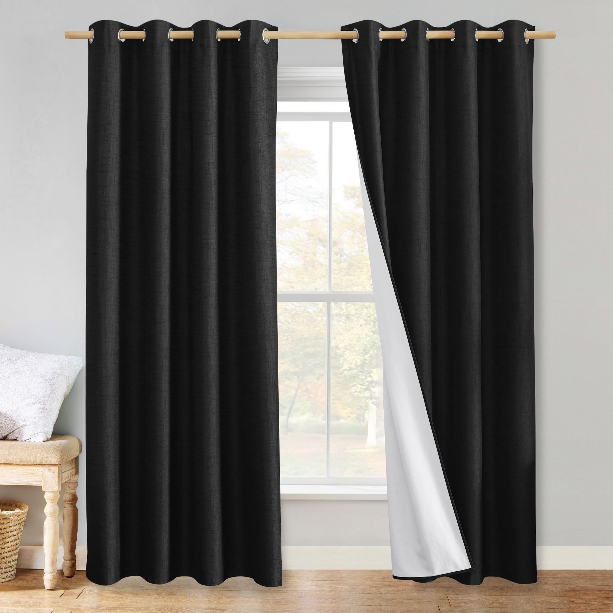 Black linen blackout curtains with grommets, with one panel pulled back to show the white blackout liner.
