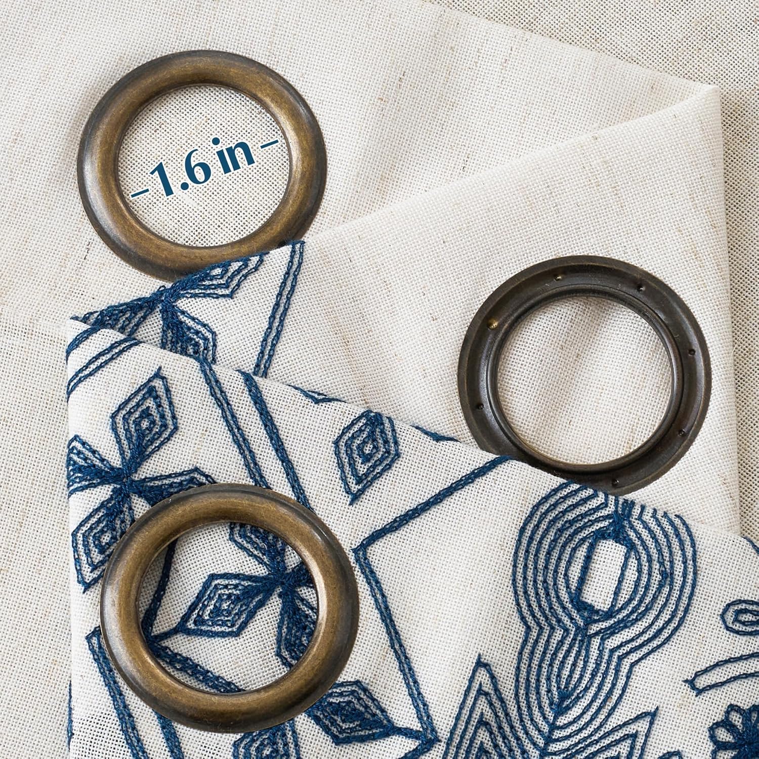 Three antique bronze 1.6 inch curtain rings on natural fabric with blue geometric embroidery.