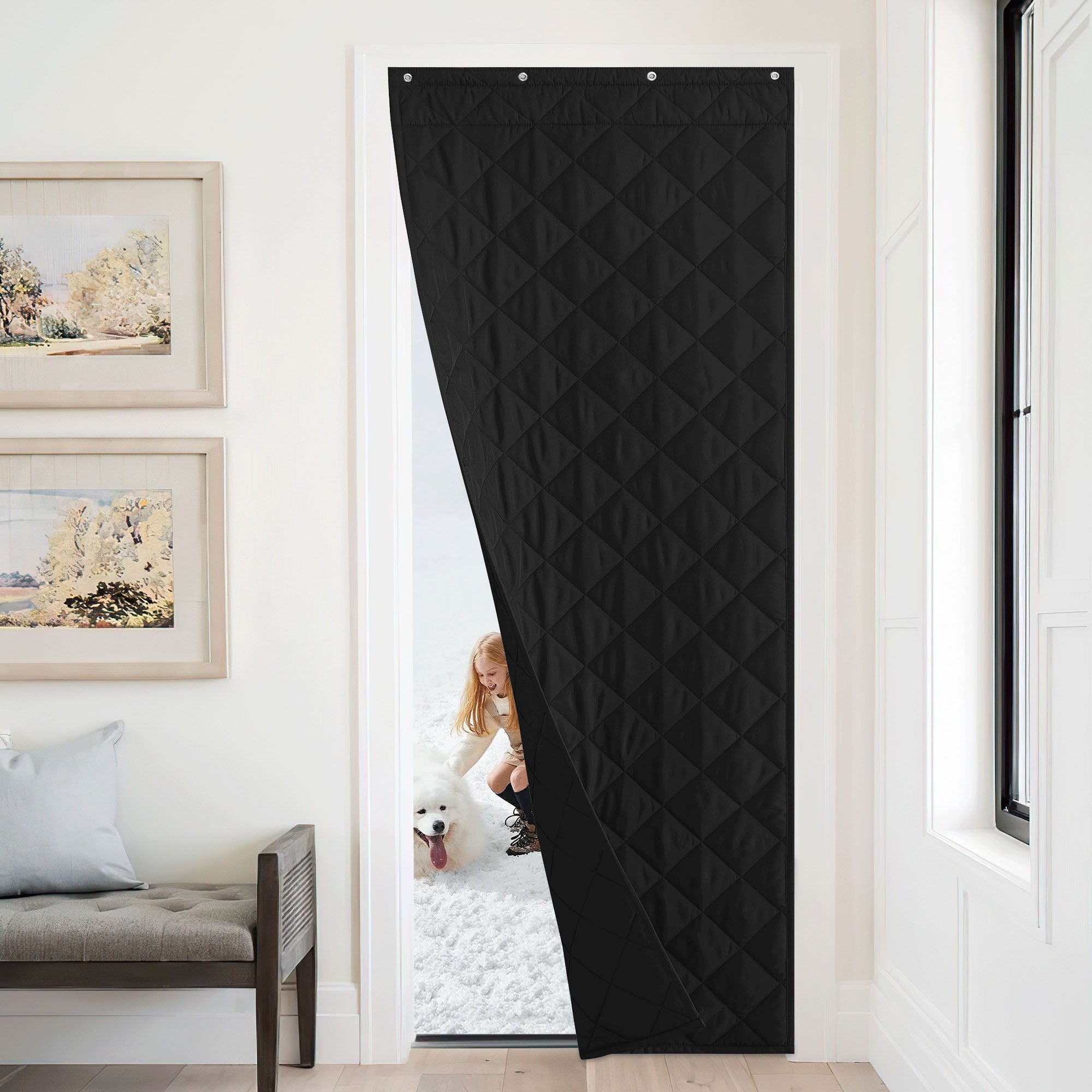 A black quilted insulated door curtain is shown partially open, blocking the cold from a snowy exterior where a girl and dog play.