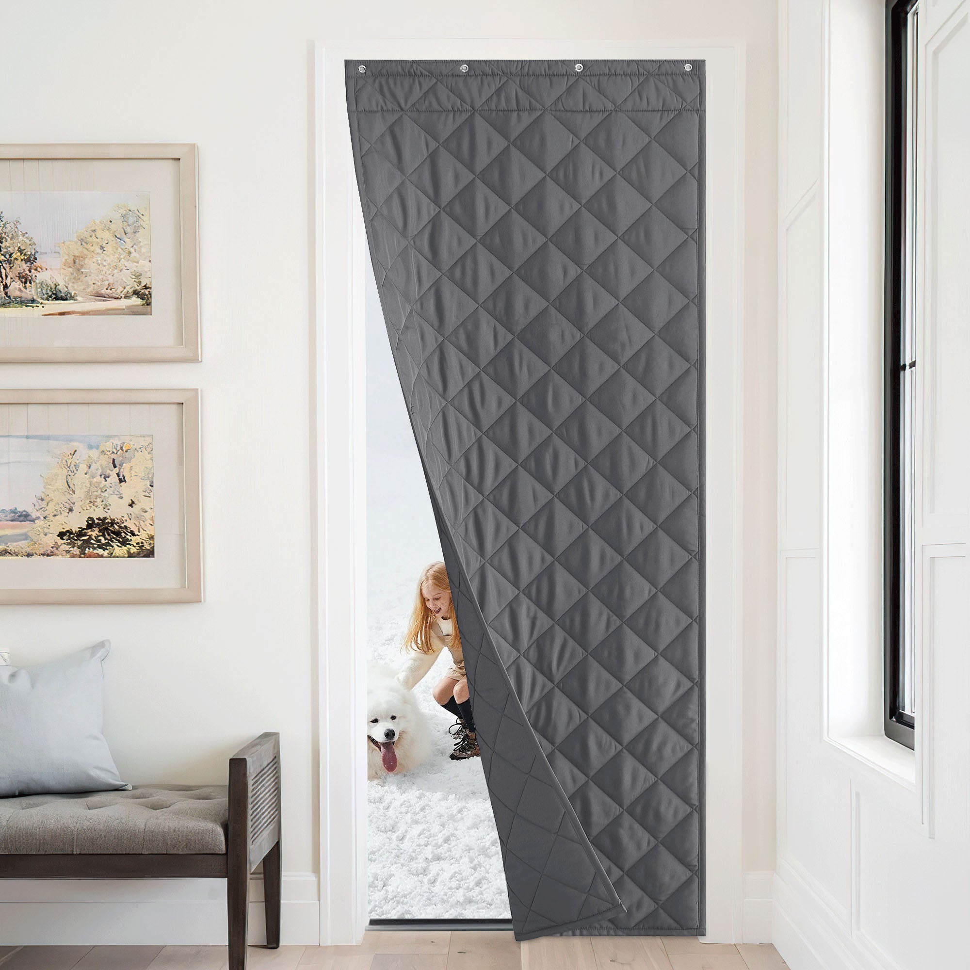 Gray quilted insulated door curtain blocks the cold from outside, where a girl and a dog play in the snow.