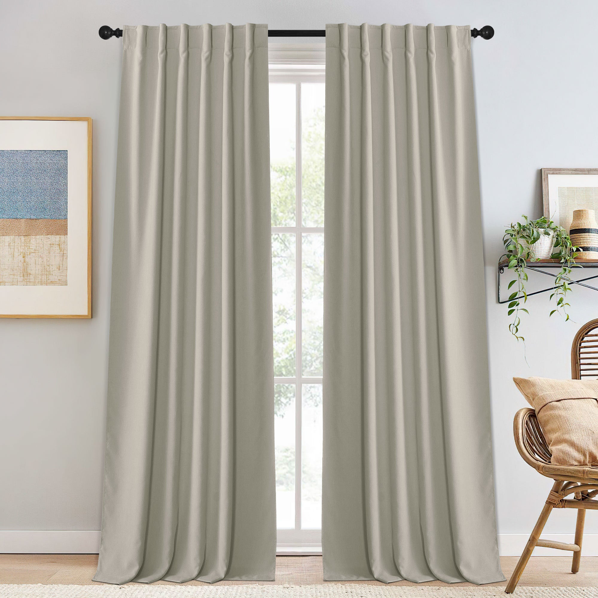 Full view of light beige pleated chenille blackout curtains on a black rod, framing a bright window.