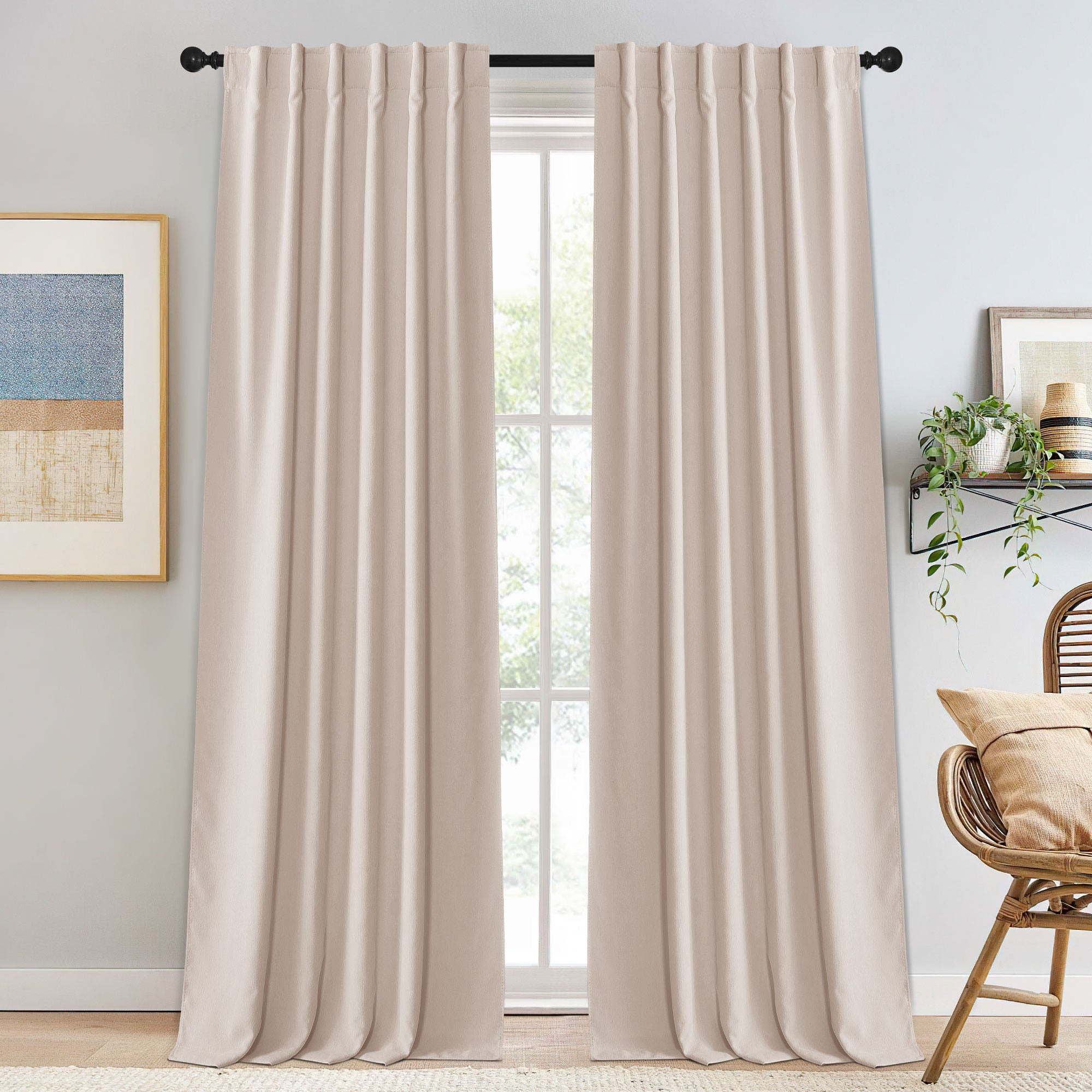 Full view of light beige chenille blackout curtains on a black rod, framing a window with plants & art nearby.