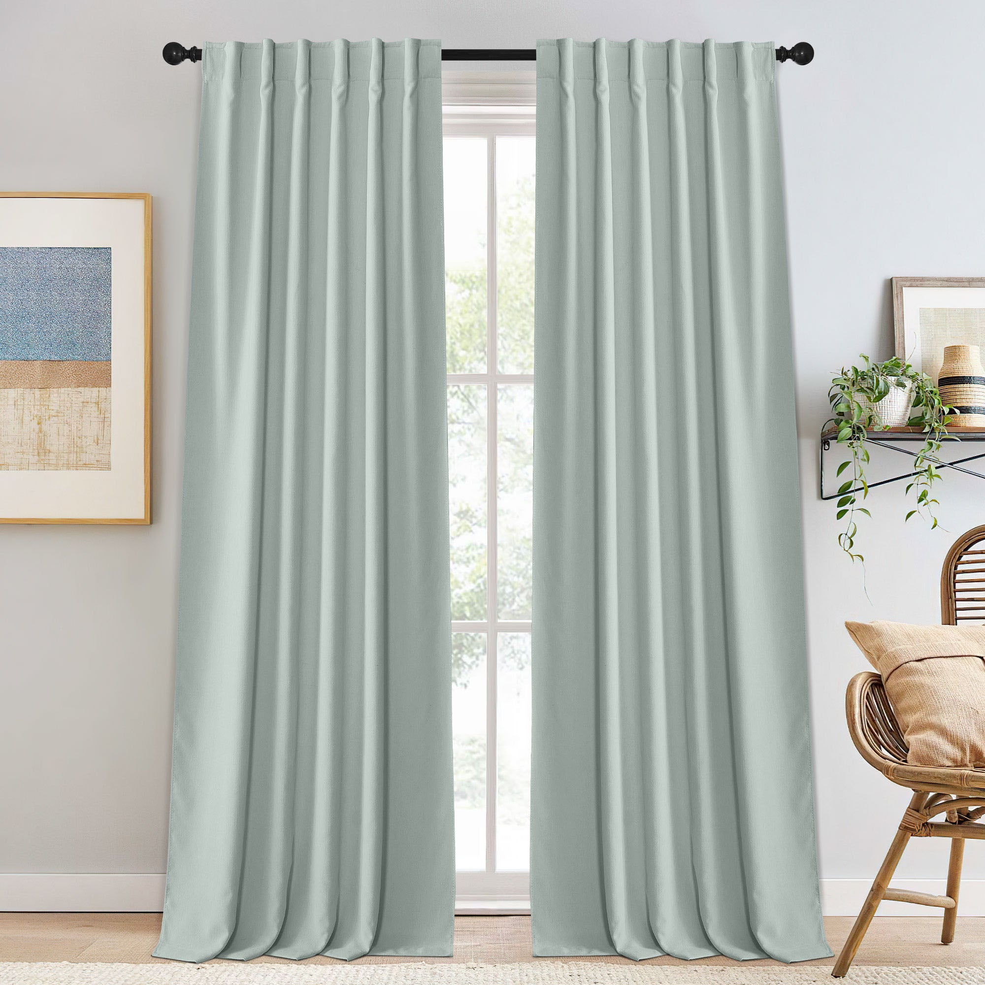 Full length light sage chenille blackout curtains on a black rod, framing a bright window, showcasing soft texture and elegant drape.