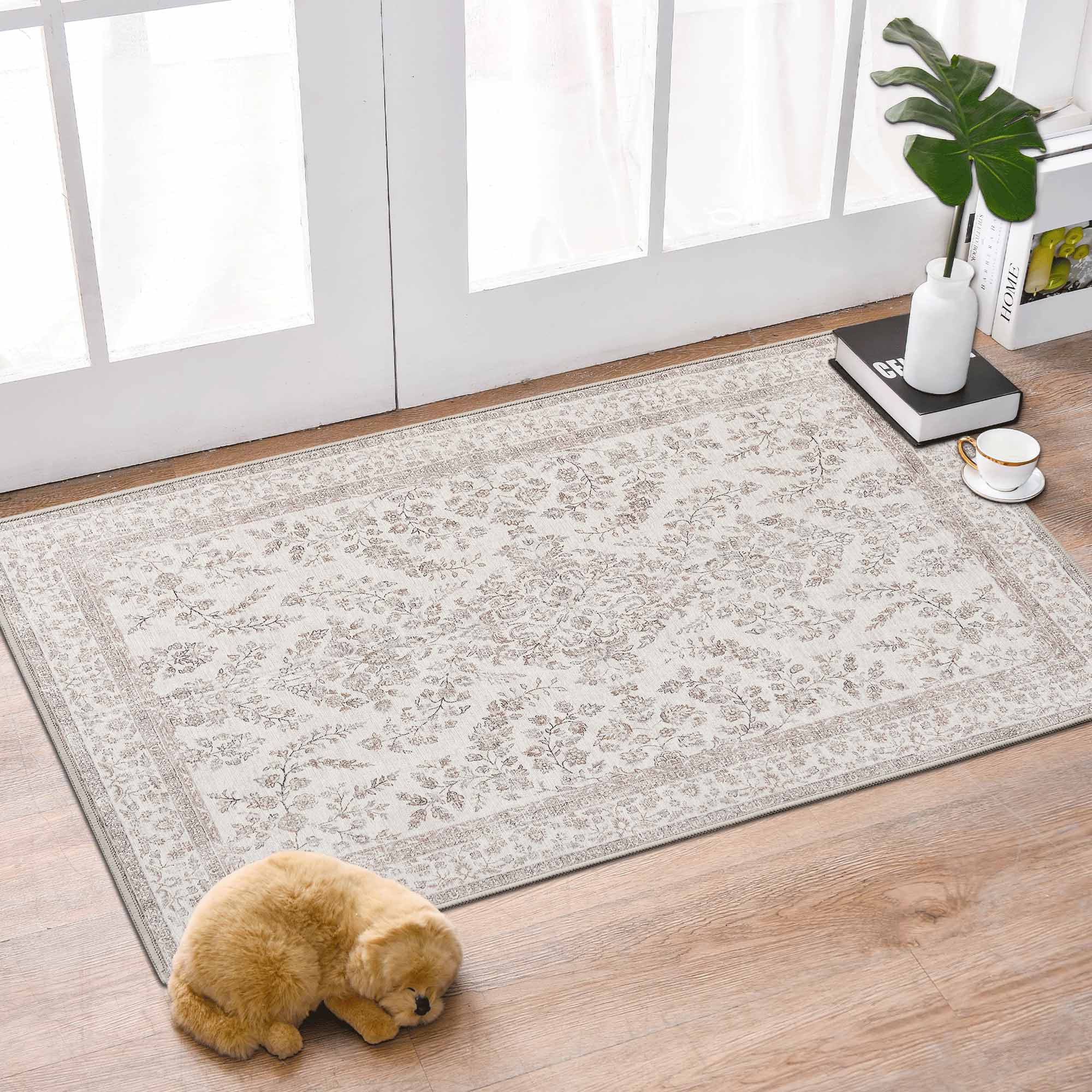 Light chenille area rug with a delicate floral design & decorative border on wood floor. A sleeping dog, books, & coffee cup complete the cozy scene.