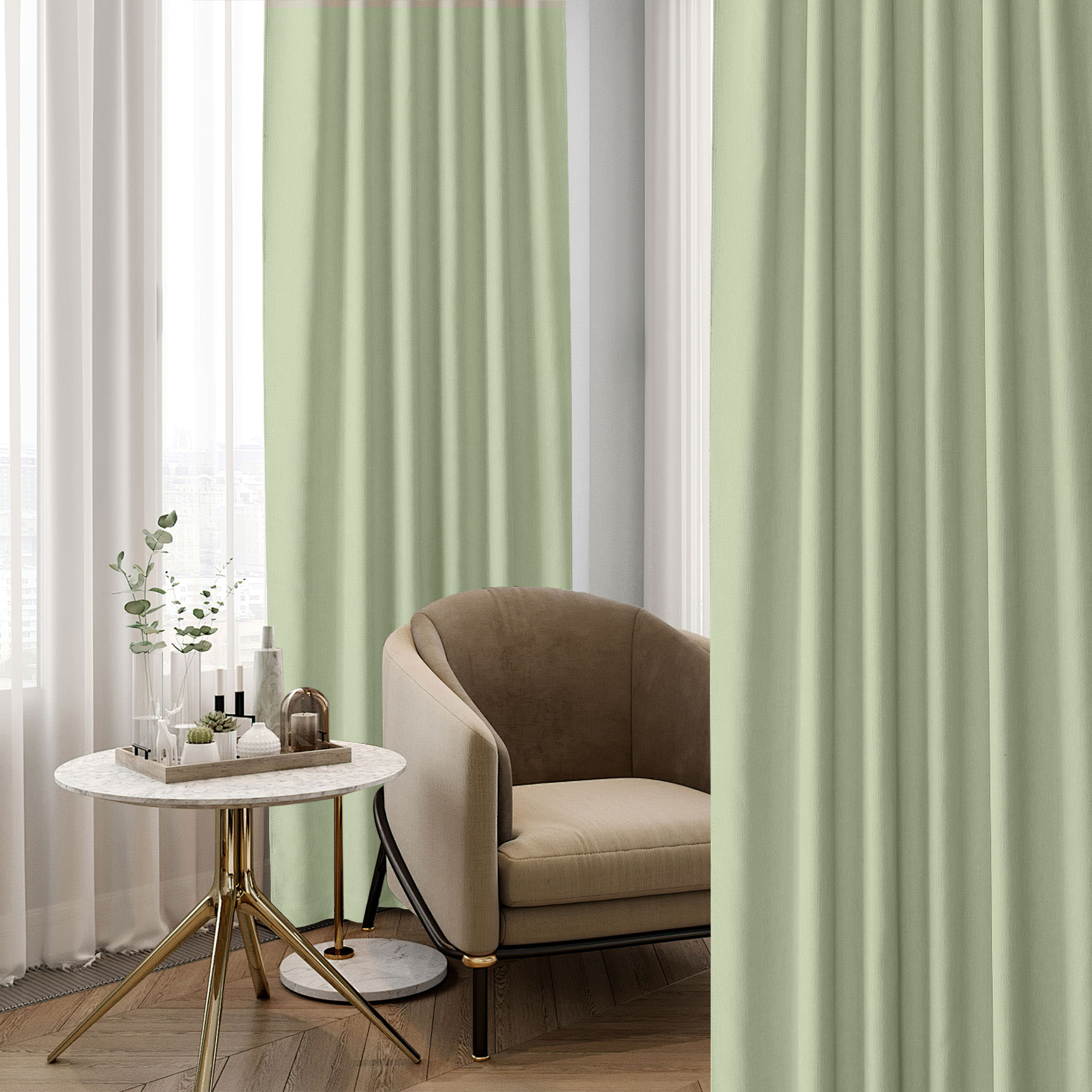 Light green chenille blackout curtains with natural folds, partially open to reveal a window and white sheers, next to a stylish armchair and side table.