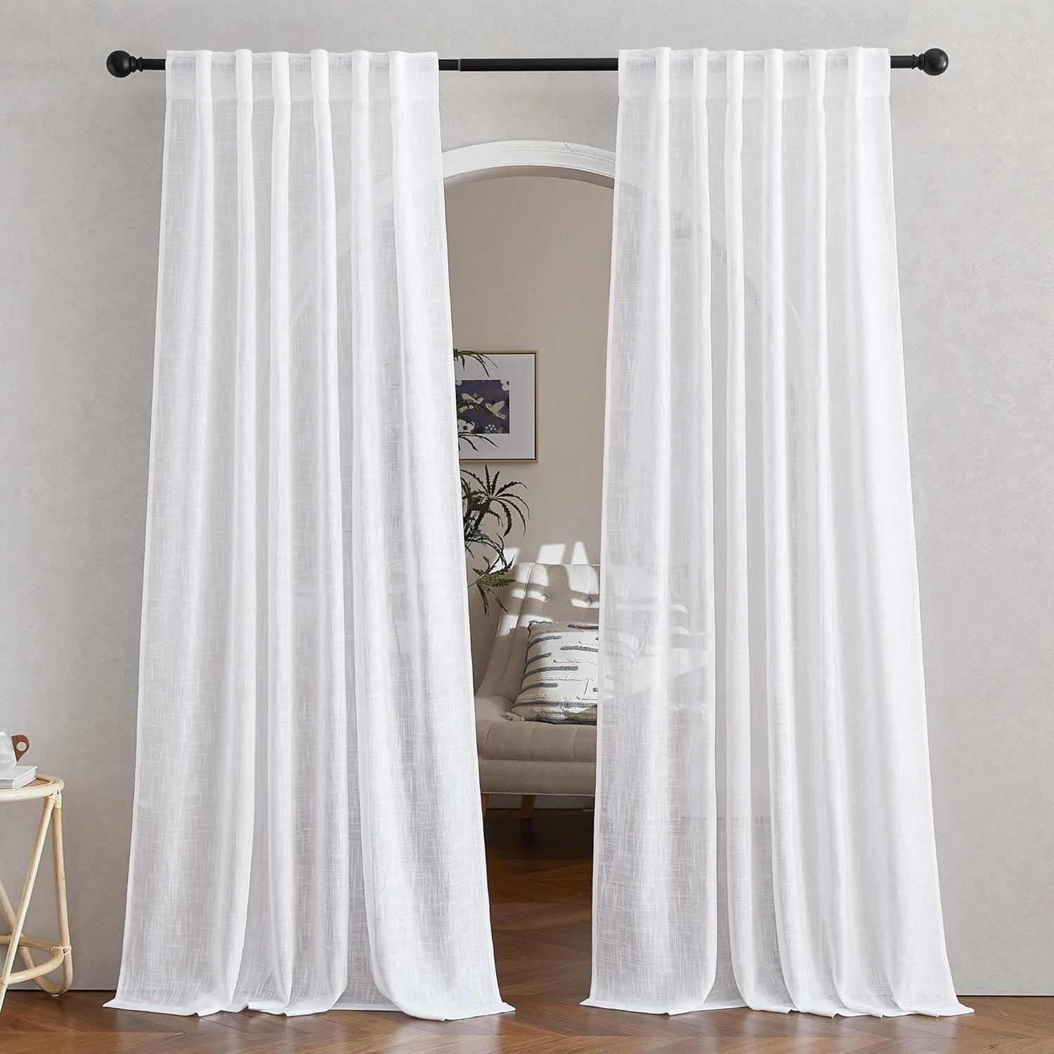 A pair of white faux linen semitransparent sheer curtains on a black rod, parted to reveal an arched doorway.