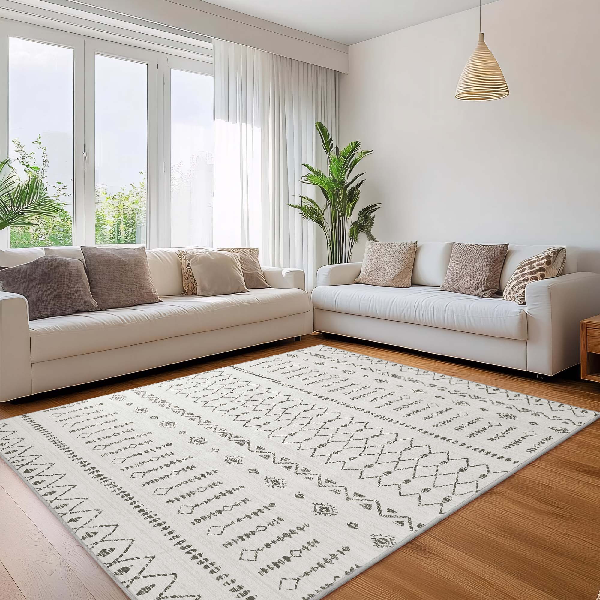 Large Starry Sand faux wool rug with grey geometric patterns centered on a wooden floor in a bright living room with white sofas.