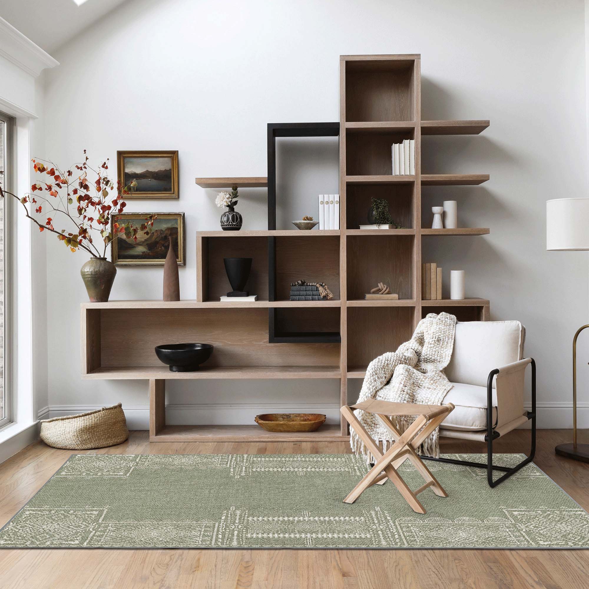 Sage green faux wool rug with white geometric patterns on a wood floor, complementing a modern living room with shelving and an armchair.