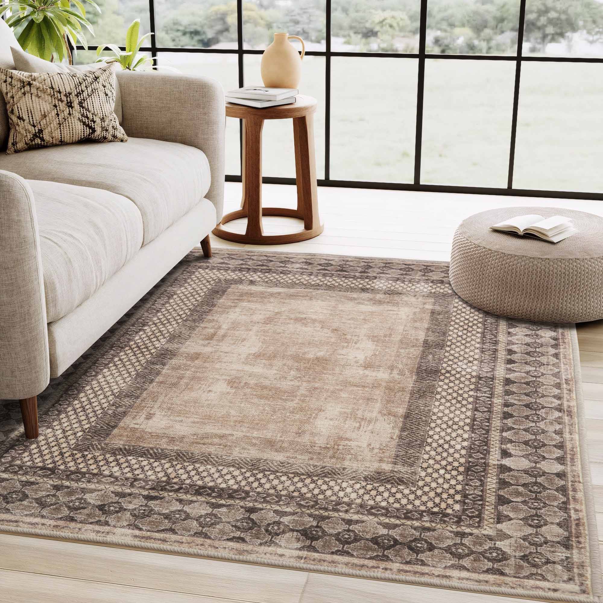 Distressed beige faux wool rug with intricate tribal border patterns, shown in a cozy living room setting with couch and pouf.