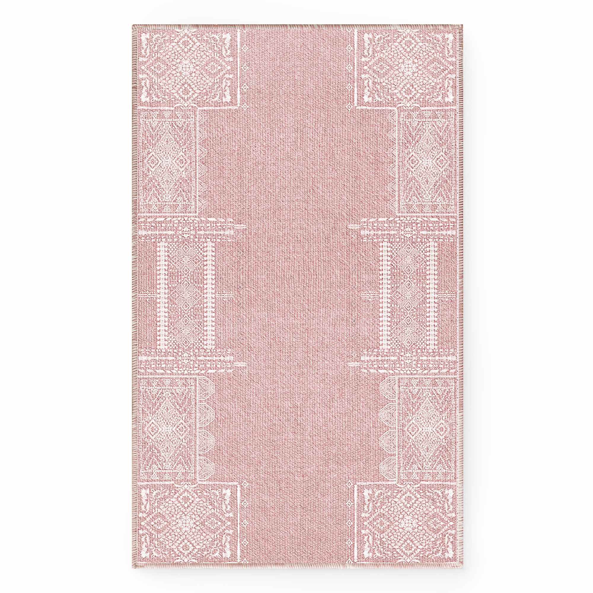 Full overhead view of a pink faux wool rug with intricate white geometric and floral patterns along the borders, showing woven texture.