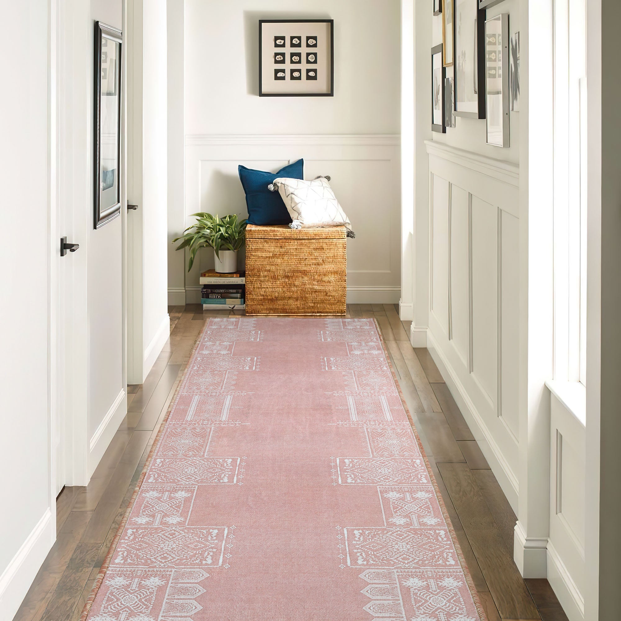 Pink faux wool runner rug with white patterns on a hardwood hallway floor, complemented by wainscoting, framed art, and basket decor.