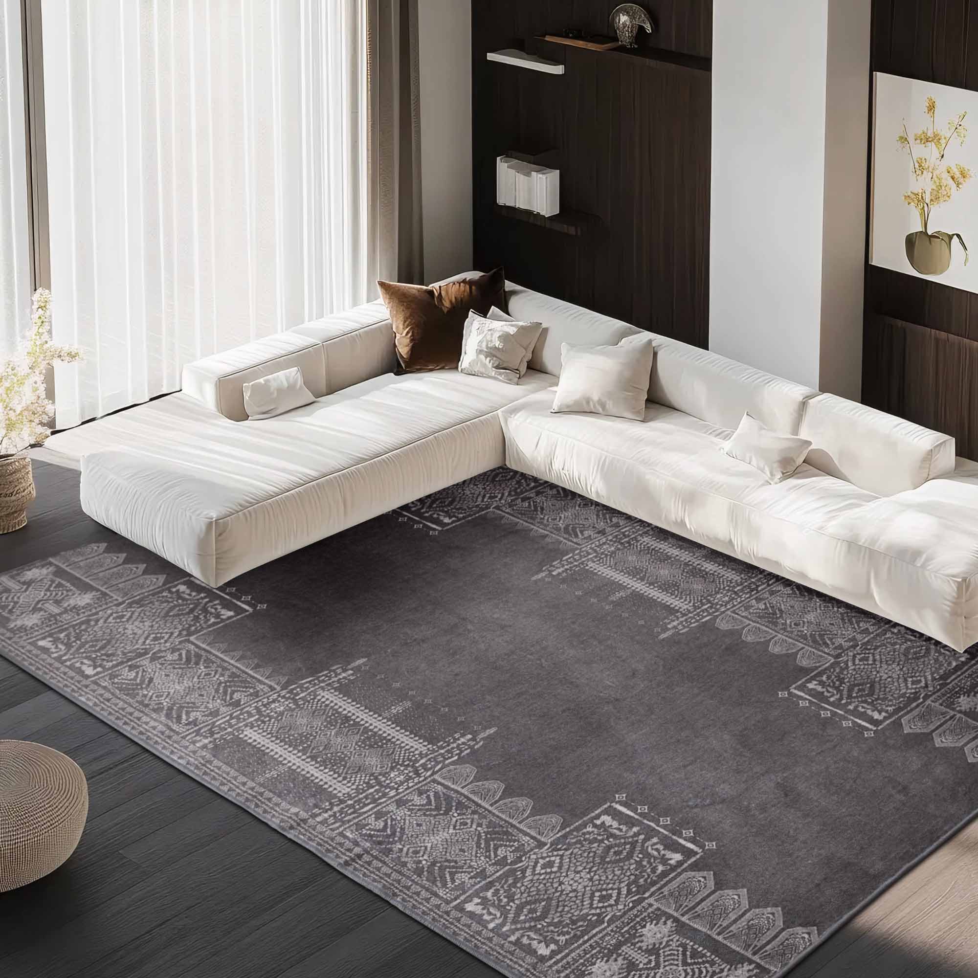 Large dark grey faux wool rug with intricate light grey patterns in a modern living room under a white sectional sofa.