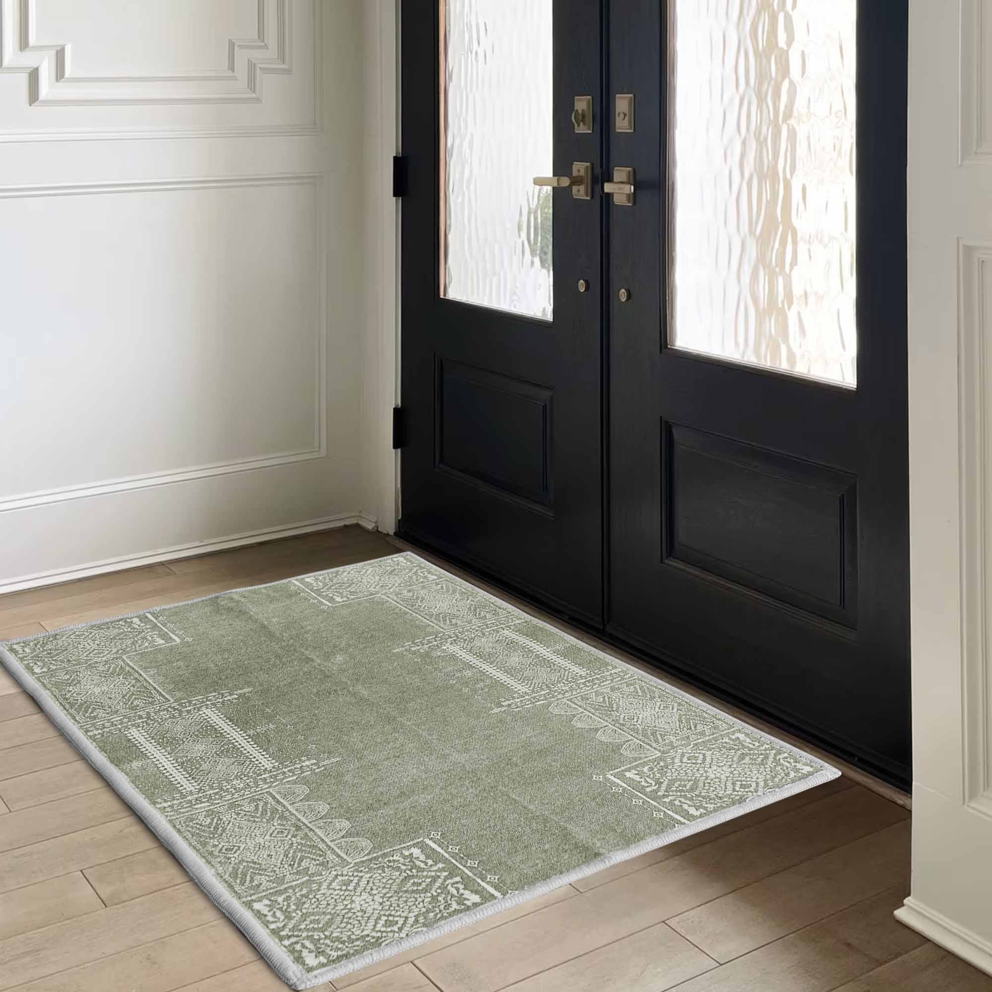 Green faux wool rug with intricate white pattern on a wooden floor in an entryway, in front of a black door and white paneling.