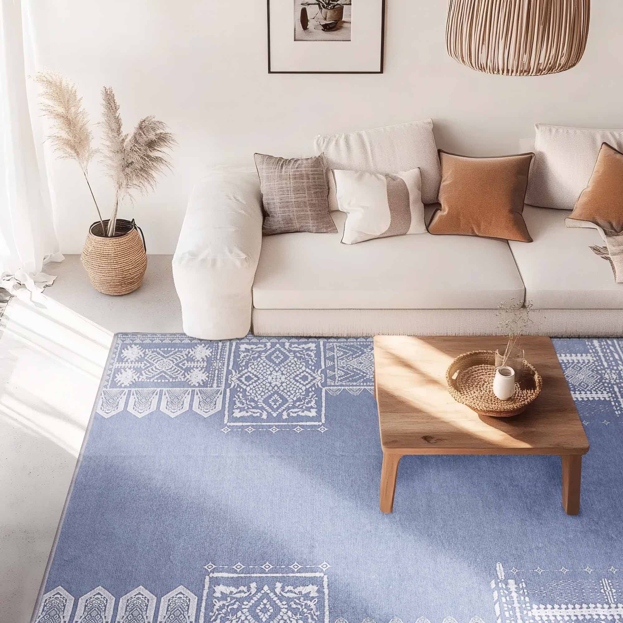 Periwinkle blue Faux Wool Rug with white geometric and tribal patterns on a concrete floor under a light sofa and wooden coffee table.