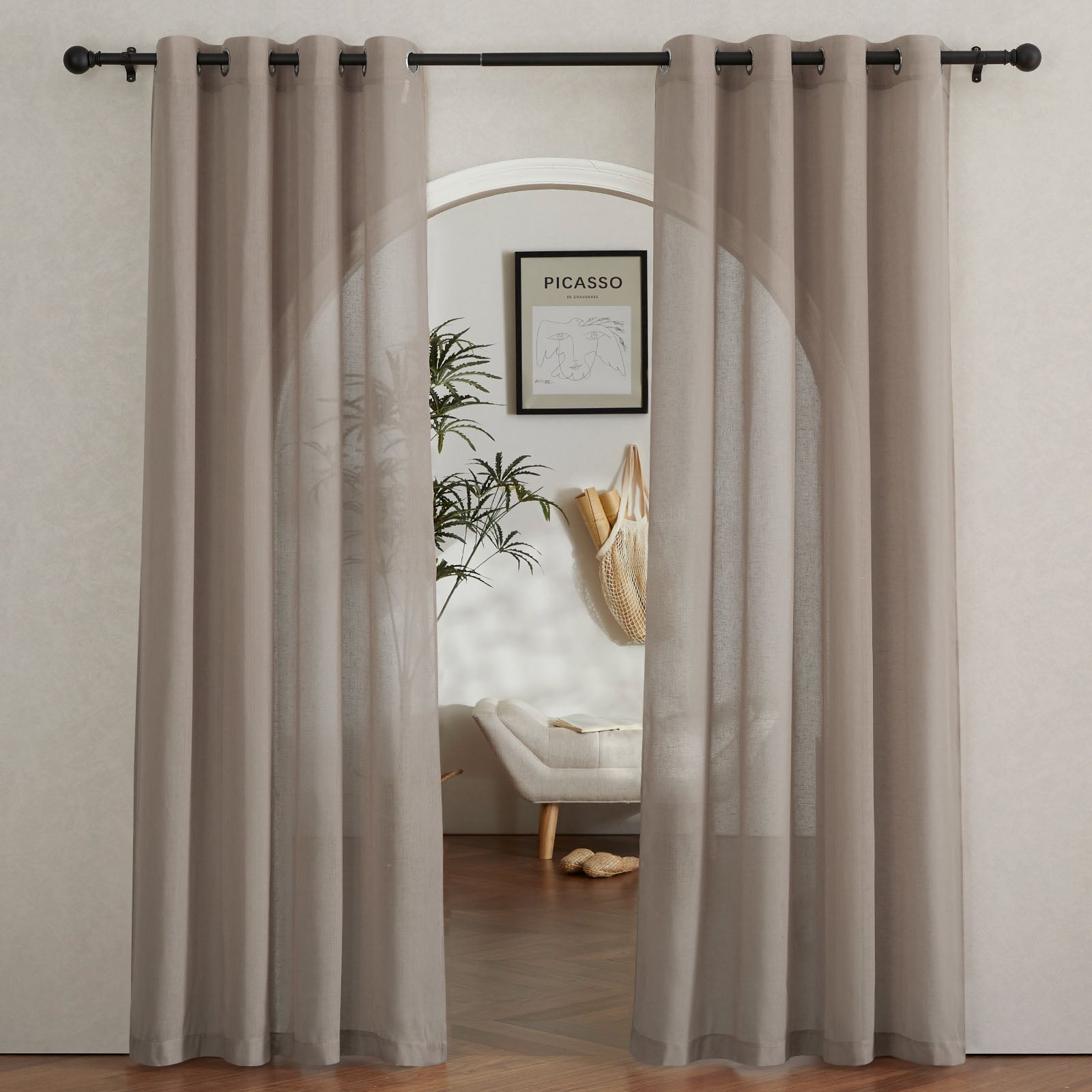 A pair of taupe faux linen sheer curtains with grommet tops framing an arched doorway, filtering soft light into the room.