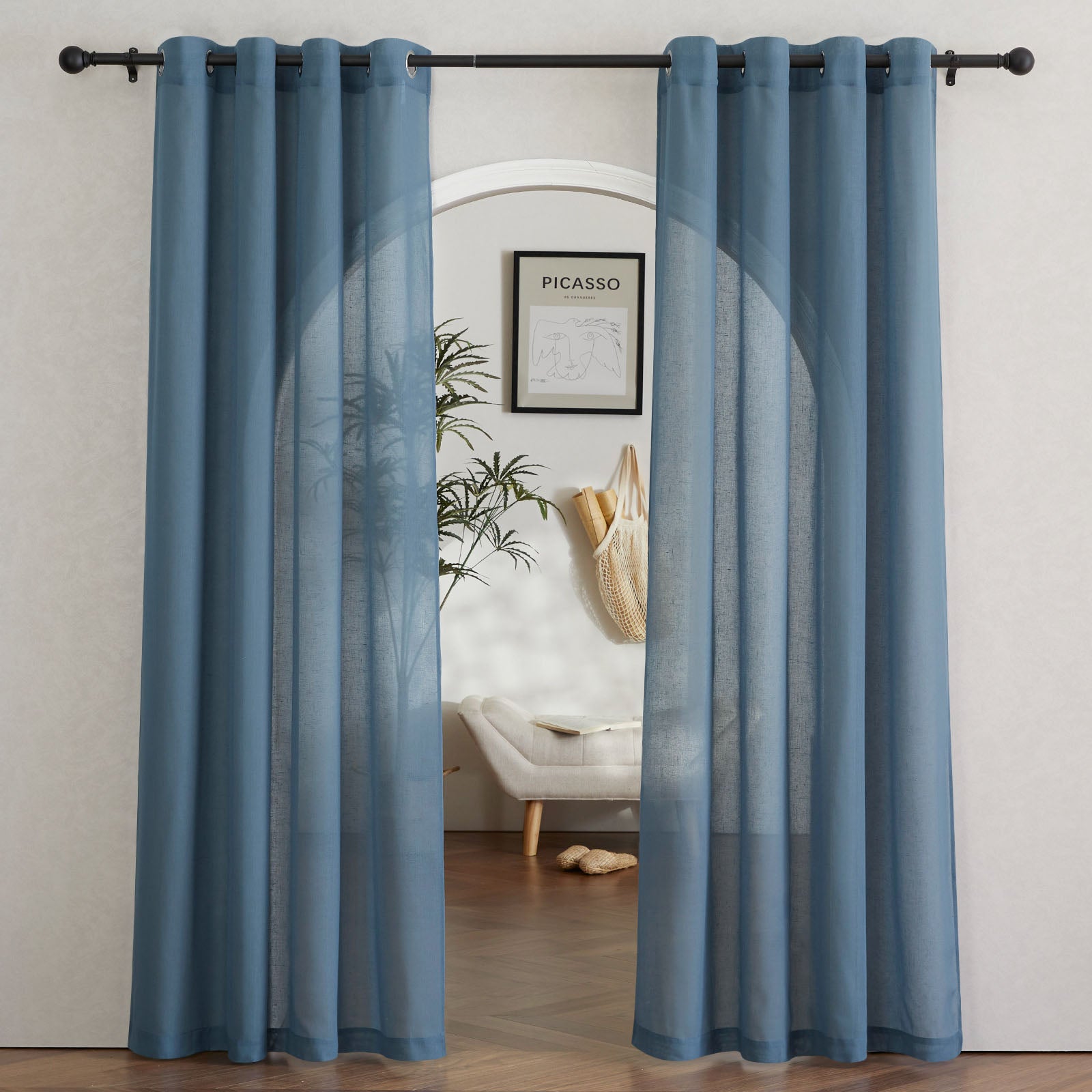 A pair of blue faux linen sheer curtains with grommet tops hanging on a black rod, framing an arched entryway.