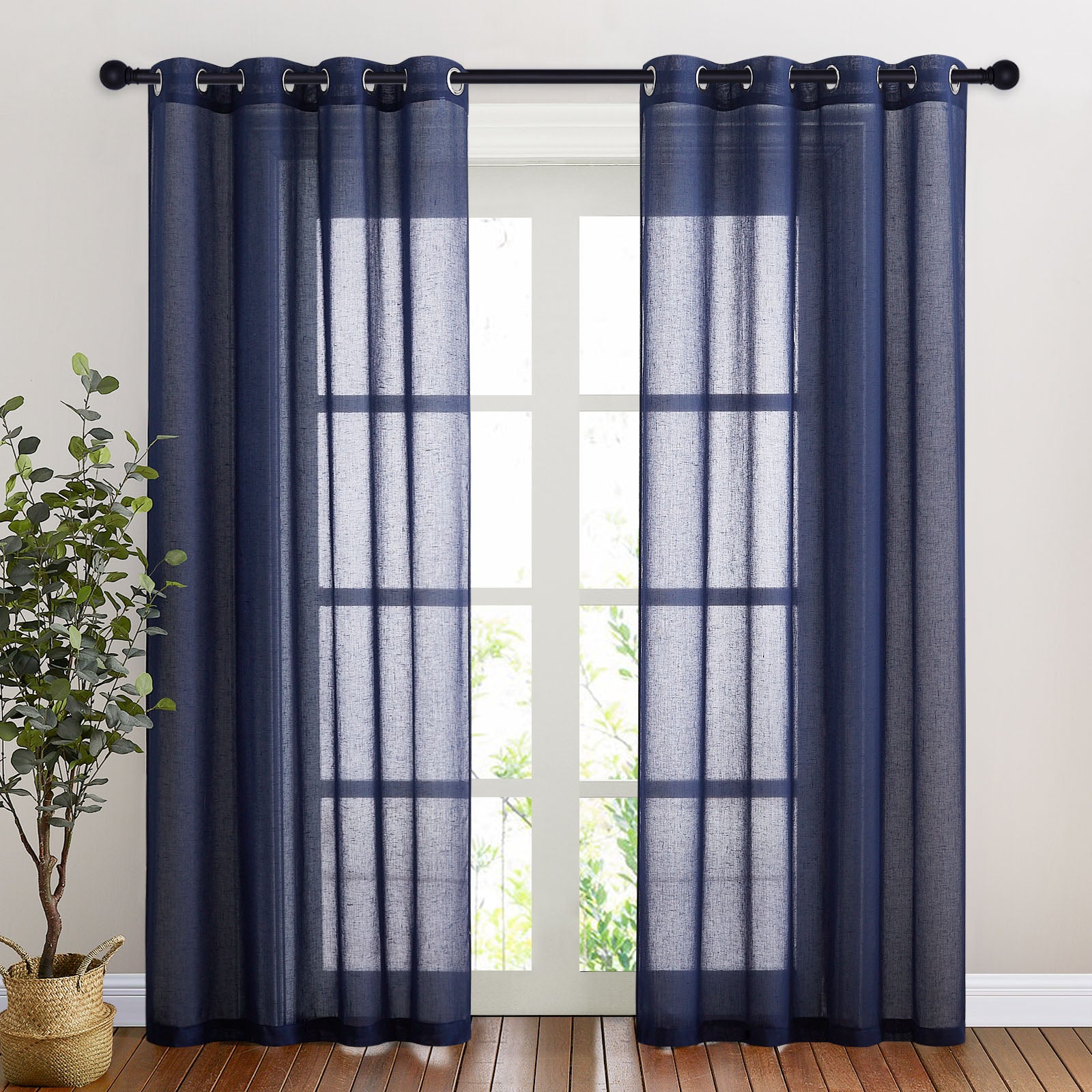 Navy blue faux linen sheer curtains with silver grommets hung on a rod, filtering daylight through a tall window in a room.