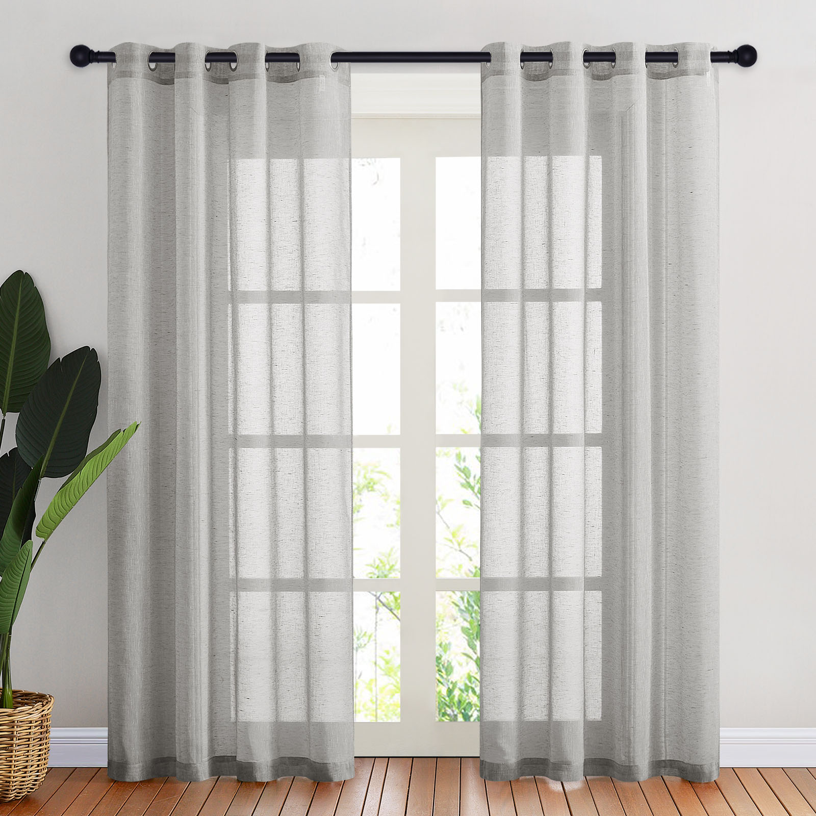A pair of grey faux linen sheer curtains with metal grommets filtering sunlight over a tall window in a bright room.