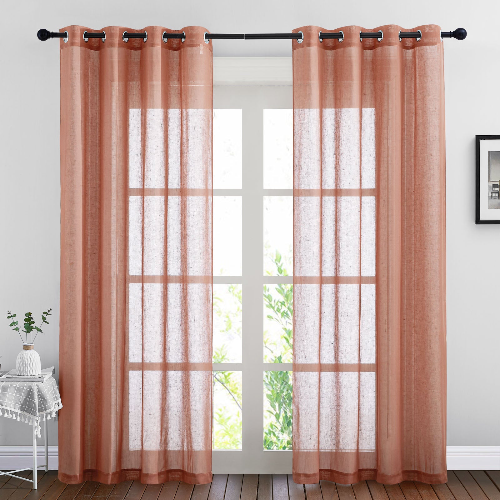 Pair of dusty rose faux linen sheer curtains with grommets hanging on a rod, filtering daylight through a window.