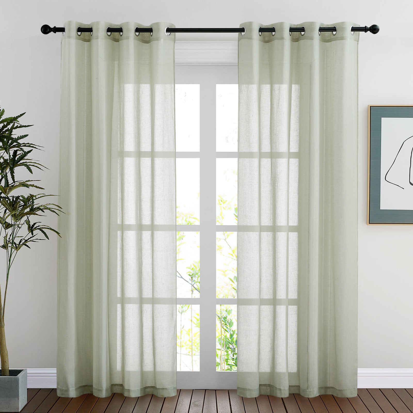 A pair of light green faux linen sheer curtains with grommets hanging on a rod over a tall window in a bright room.