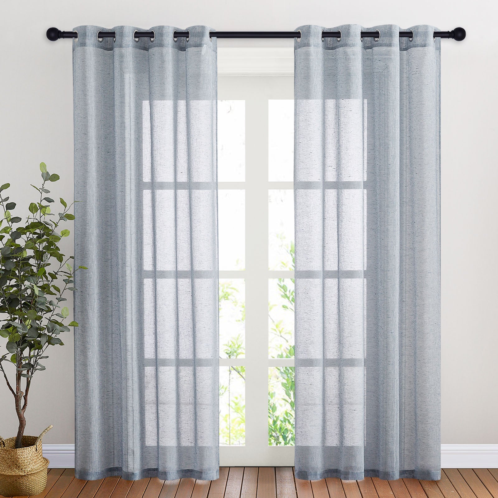 Two light blue faux linen sheer curtains with silver grommets hung on a black rod, filtering light from a large window.