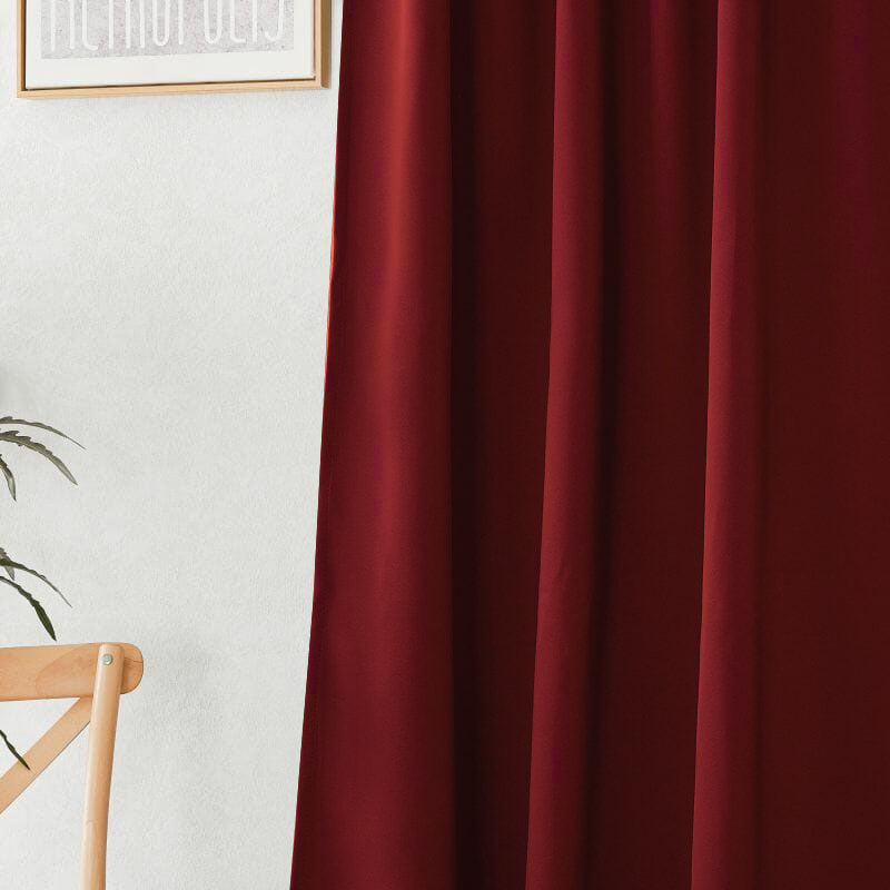 Close-up of deep red flame retardant curtains with visible folds and rich fabric texture, next to a white wall.