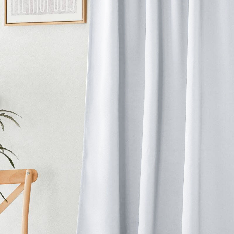 Close-up of a white flame retardant curtain, showcasing its soft fabric folds. A light wall, wooden chair, and plant are visible.