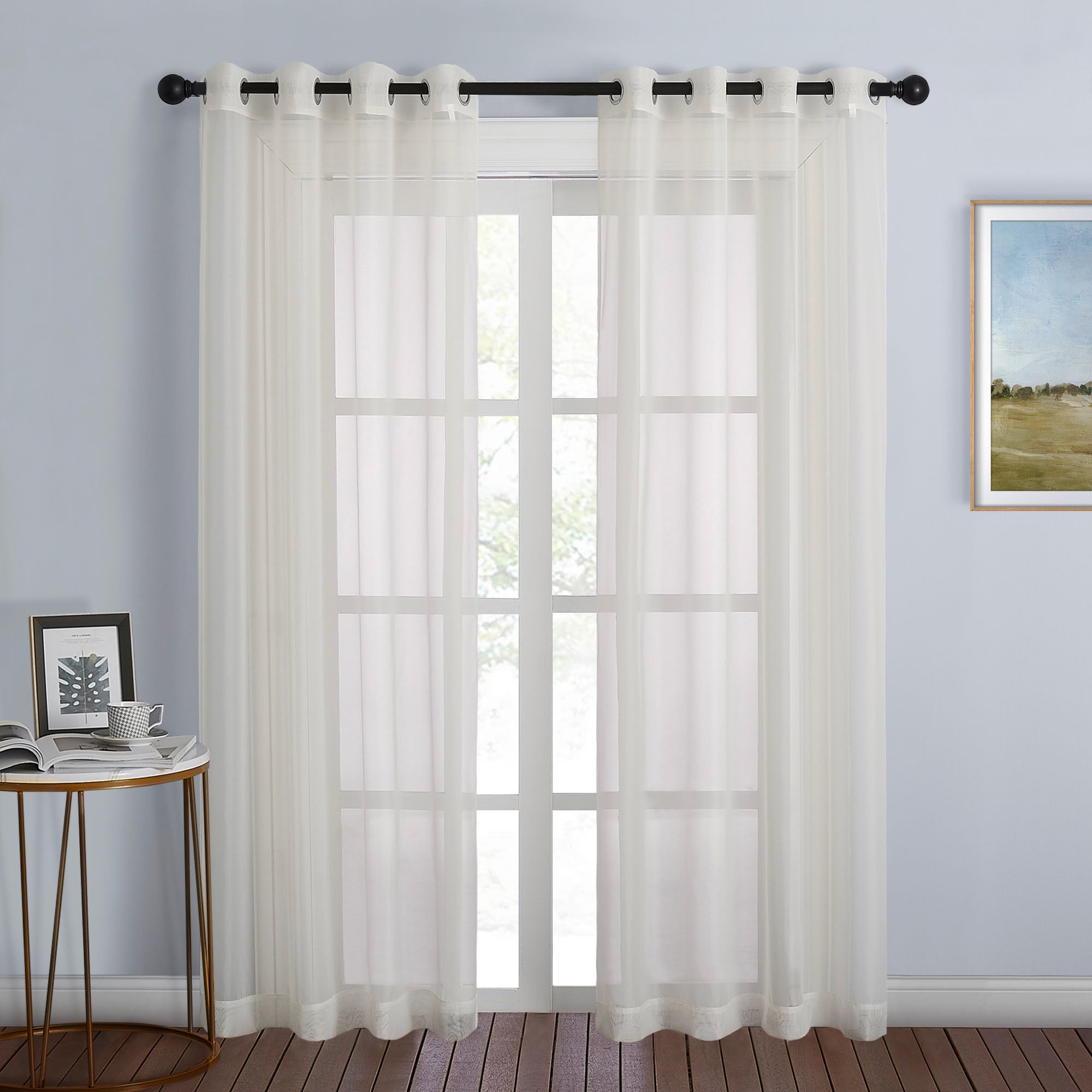 A pair of light sheer ivory curtains with black grommets hang on a rod, gently filtering light into a stylish living room.
