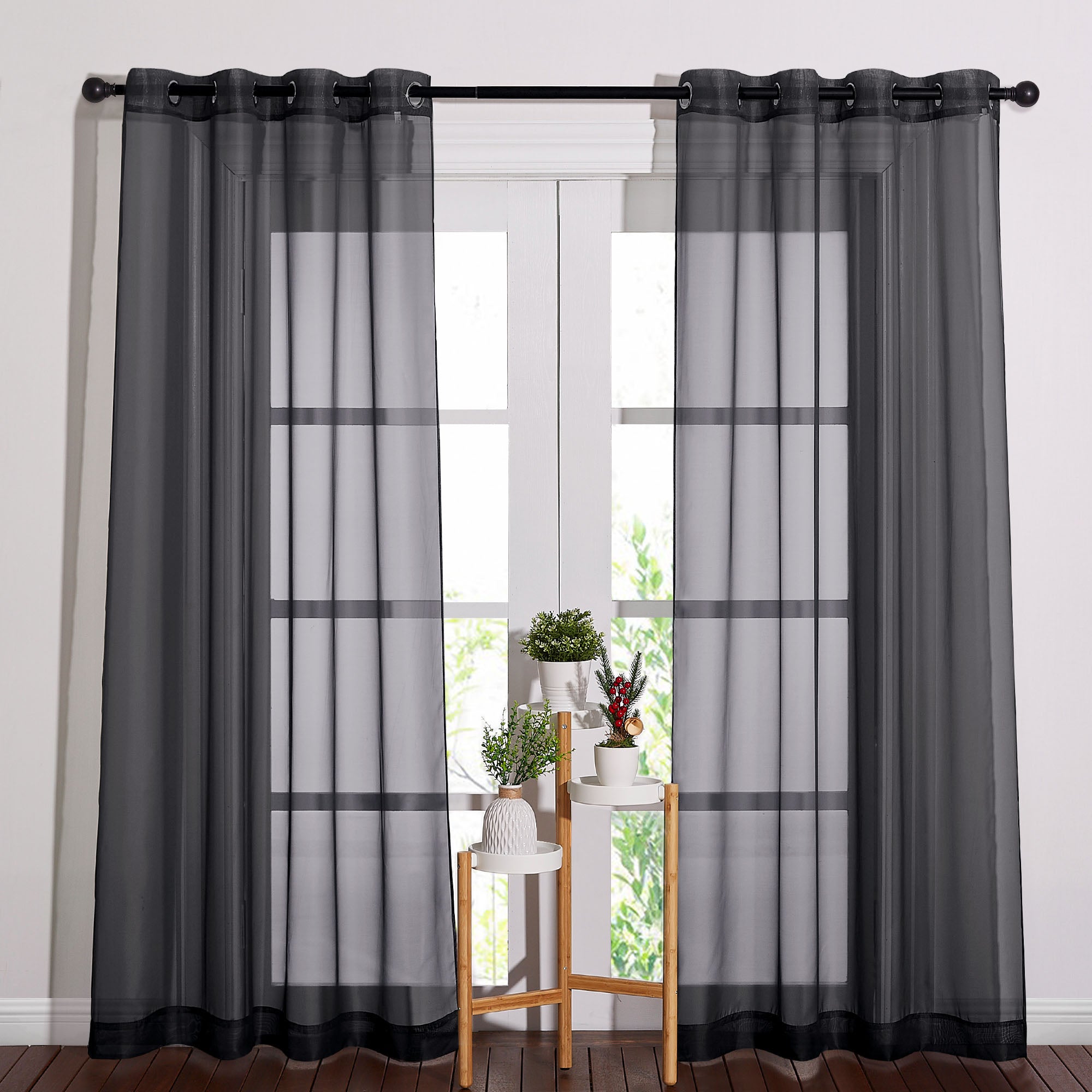 A pair of black light sheer curtains with metal grommets hanging on a rod, filtering daylight through glass doors.