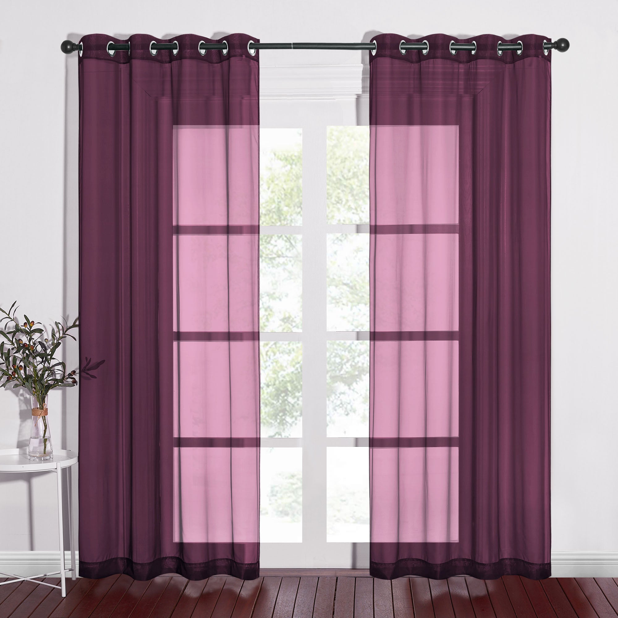 A pair of plum-colored light sheer curtains with metal grommets hanging on a black curtain rod over a window.