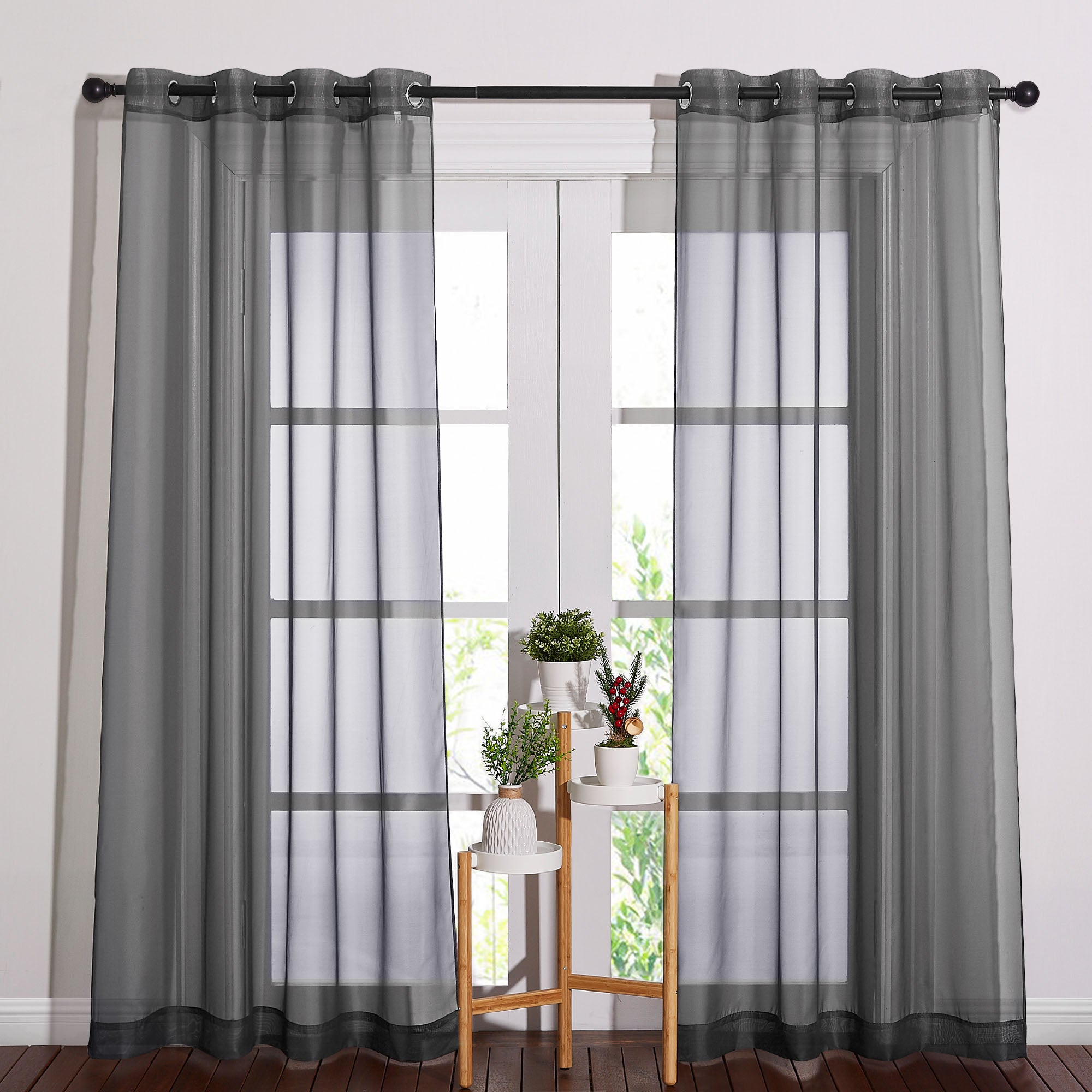 Grey sheer grommet curtains hanging on a black rod over a large window, filtering natural light into a room.