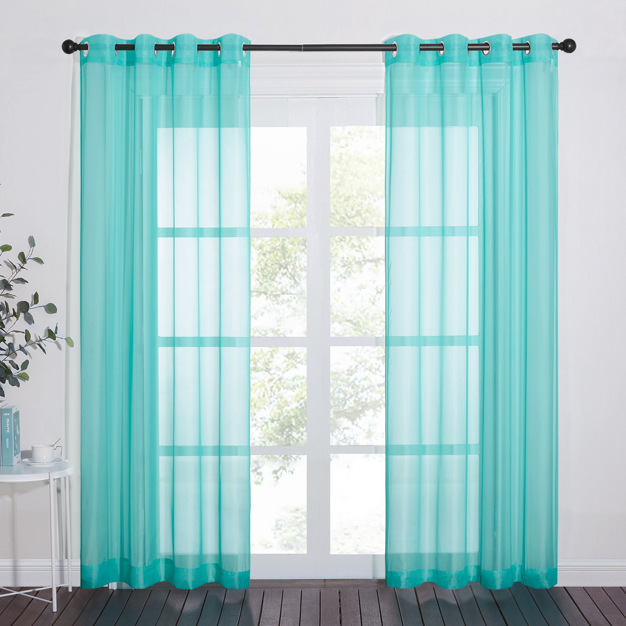 Two turquoise light sheer curtain panels with grommets hang on a rod, filtering light from a large window.