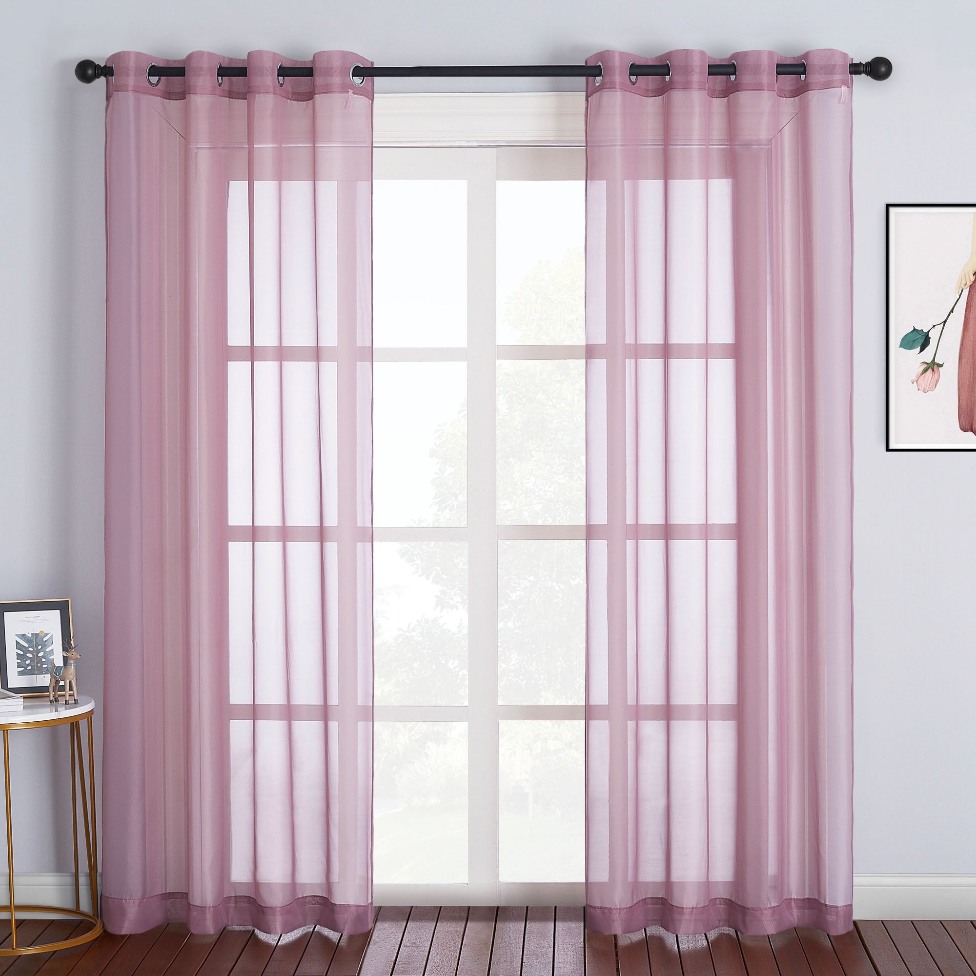 Dusty pink light sheer curtains with metal grommets hang on a rod, filtering daylight through a large window.