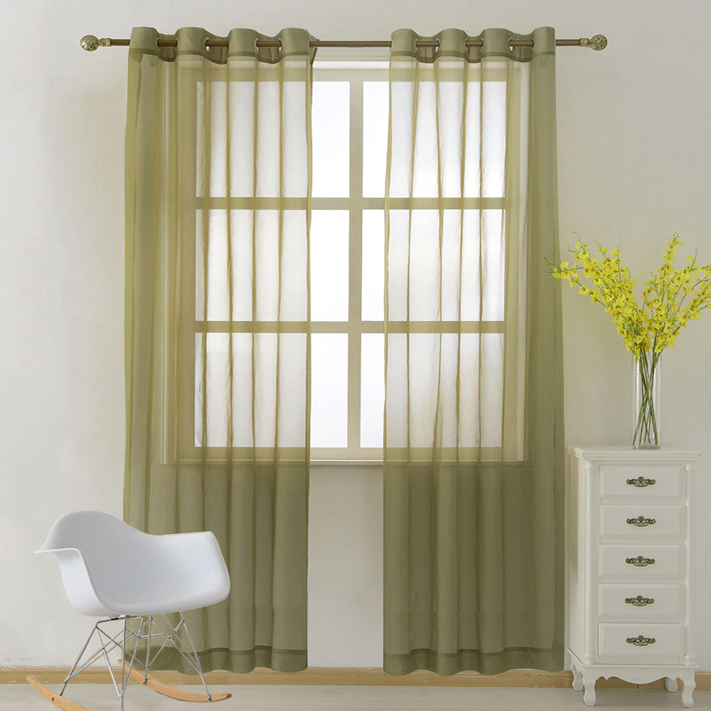 A pair of olive green light sheer curtains with grommet tops hanging over a window in a brightly lit room.
