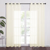 A pair of light cream sheer curtains with silver grommets on a black rod, filtering sunlight through a large window.