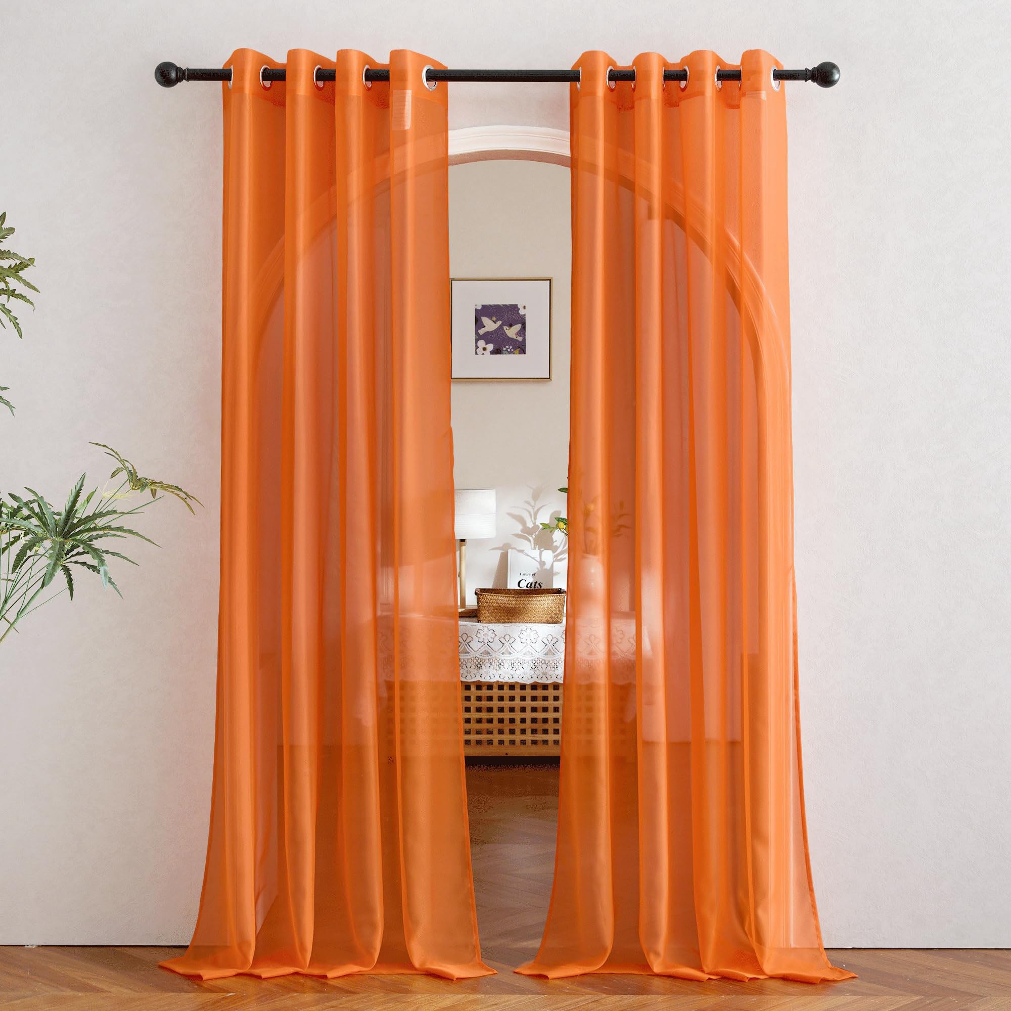 Light sheer orange curtains with silver grommets hang on a rod, framing an arched doorway and filtering light into a room.