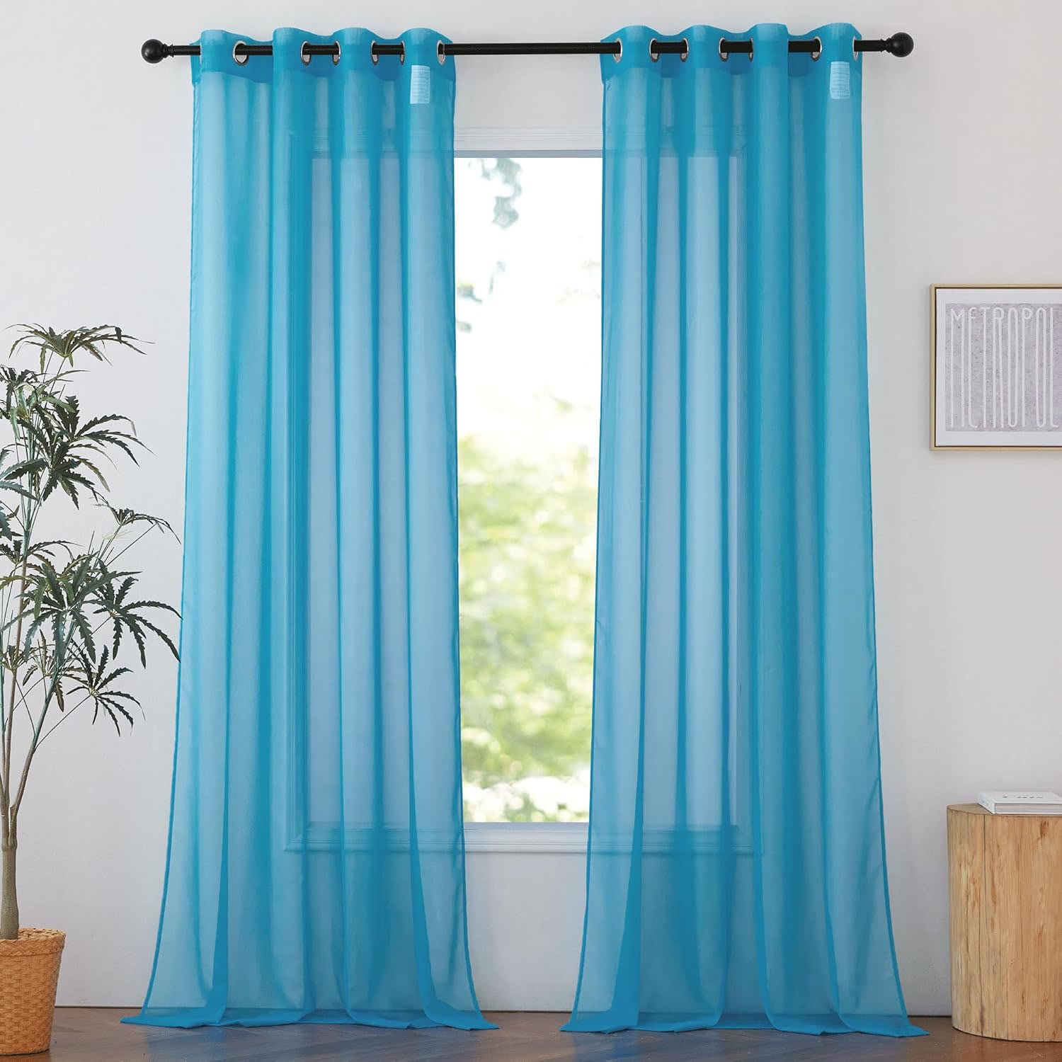 Two light turquoise sheer curtain panels with silver grommets hang on a black rod, filtering soft light from a window.