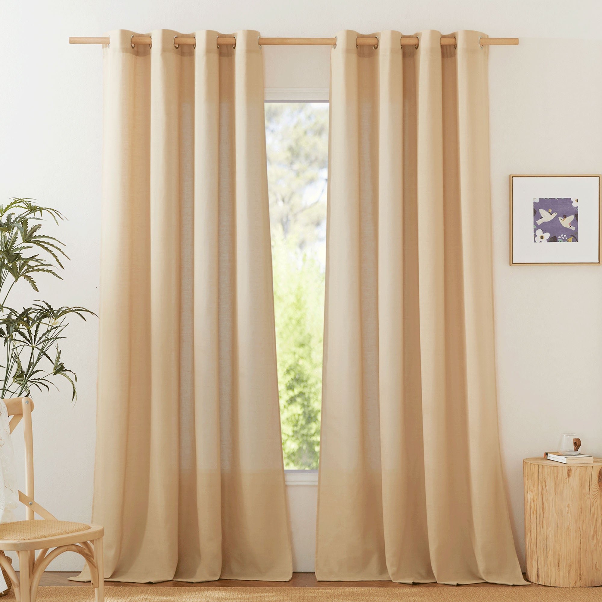 Beige linen grommet curtains hanging on a wooden rod in a brightly lit room with natural wood decor and a plant.