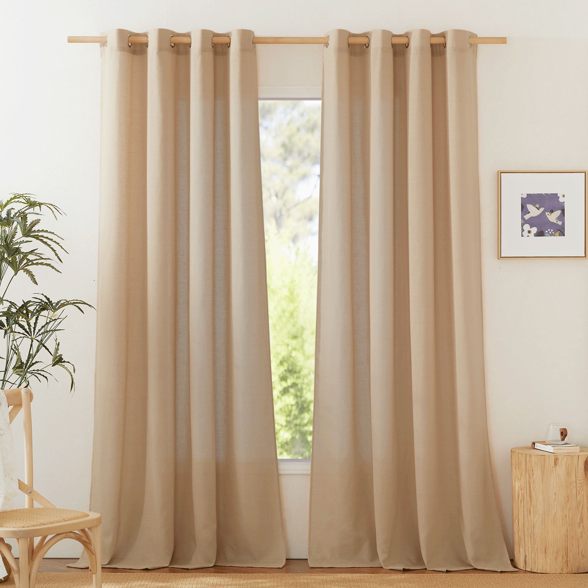 Light beige grommet-top linen curtains hanging on a wood rod, framing a sunny window in a minimalist living room setting.