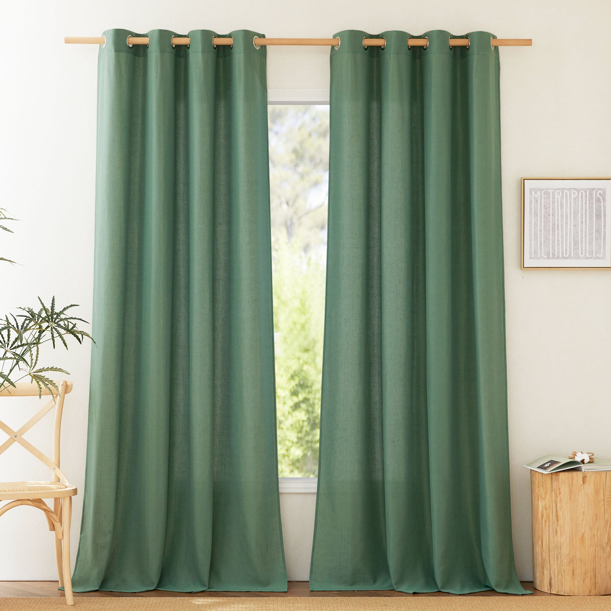 A pair of floor-length green linen curtains with silver grommets hung on a light wood rod in a sunlit room.