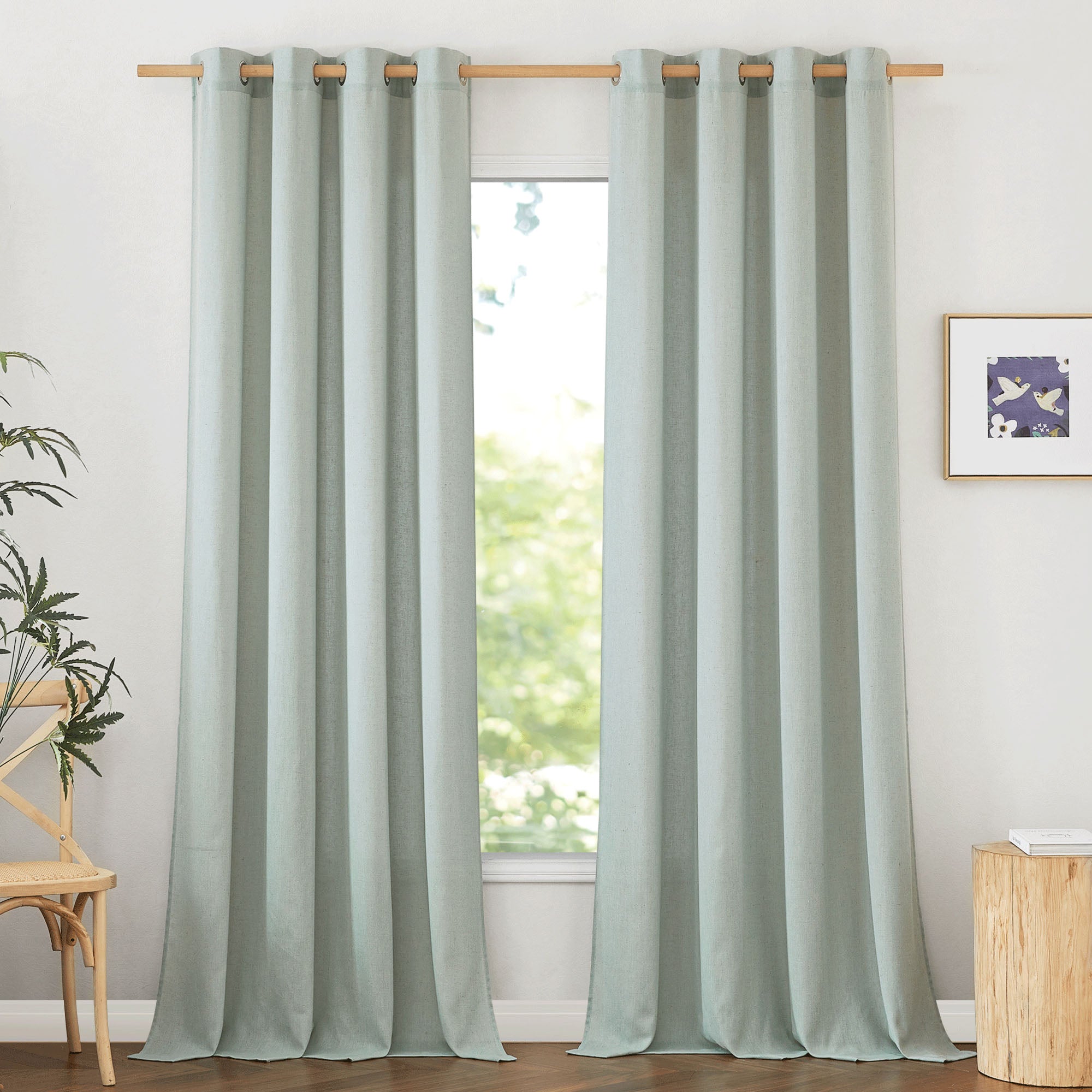A pair of light green grommet-top linen curtains hanging on a wooden rod, shown closed in front of a bright window.