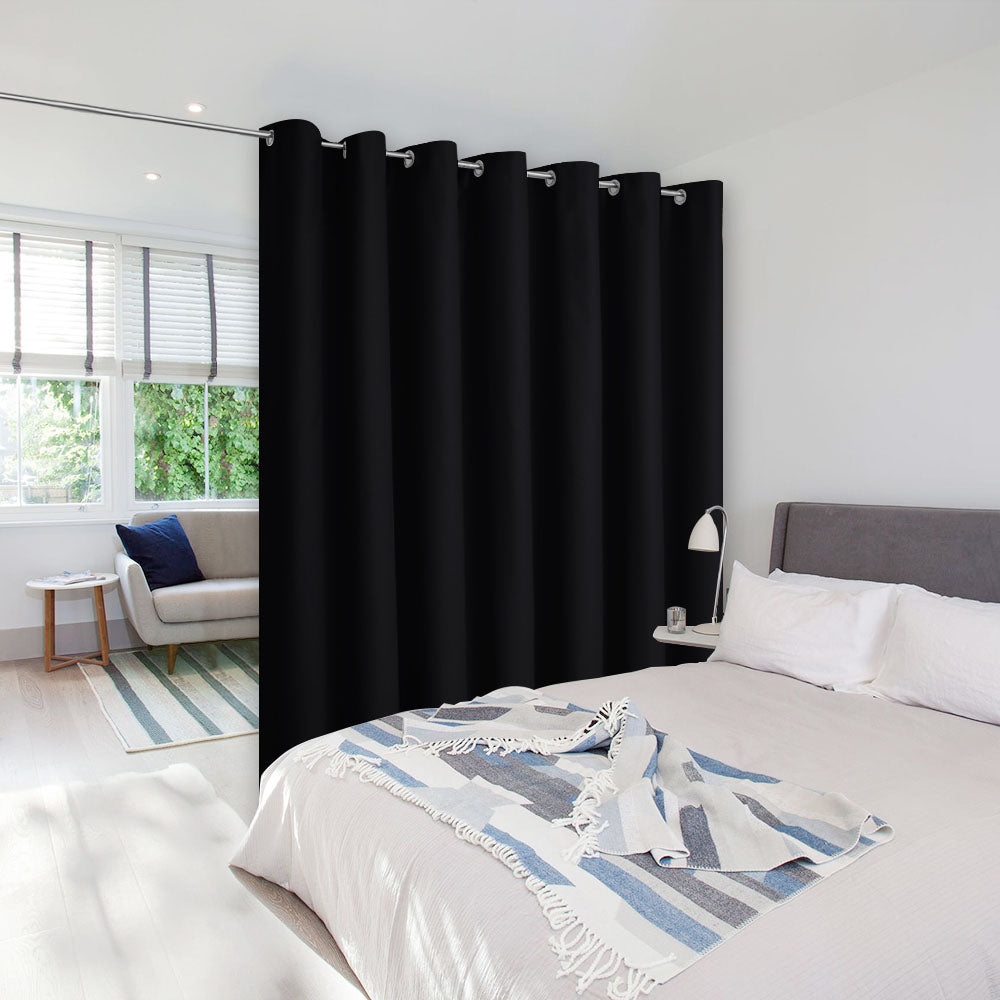 A black room divider curtain with silver grommets separating a bedroom from a living area in a bright, modern apartment.