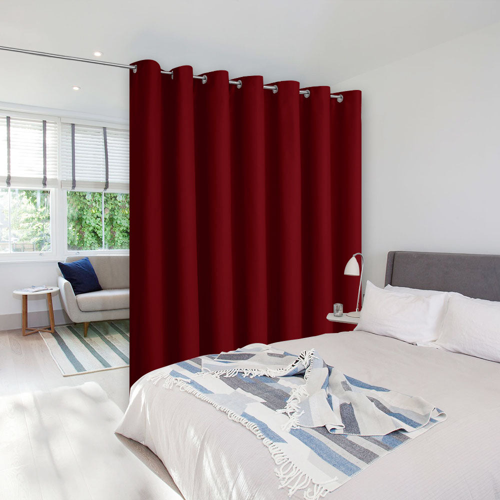 A dark red room divider curtain with silver grommets separates a bedroom area from a sunlit living space.