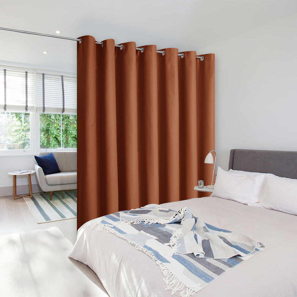 A rust-colored, grommet-top room divider curtain on a tension rod separates a bedroom area from a sunlit sitting area.