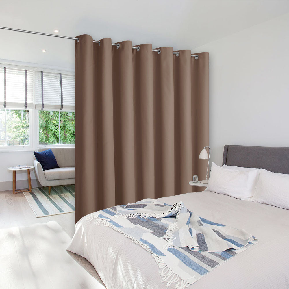 A light brown room divider curtain with silver grommets separating a bedroom from a small, bright living area.