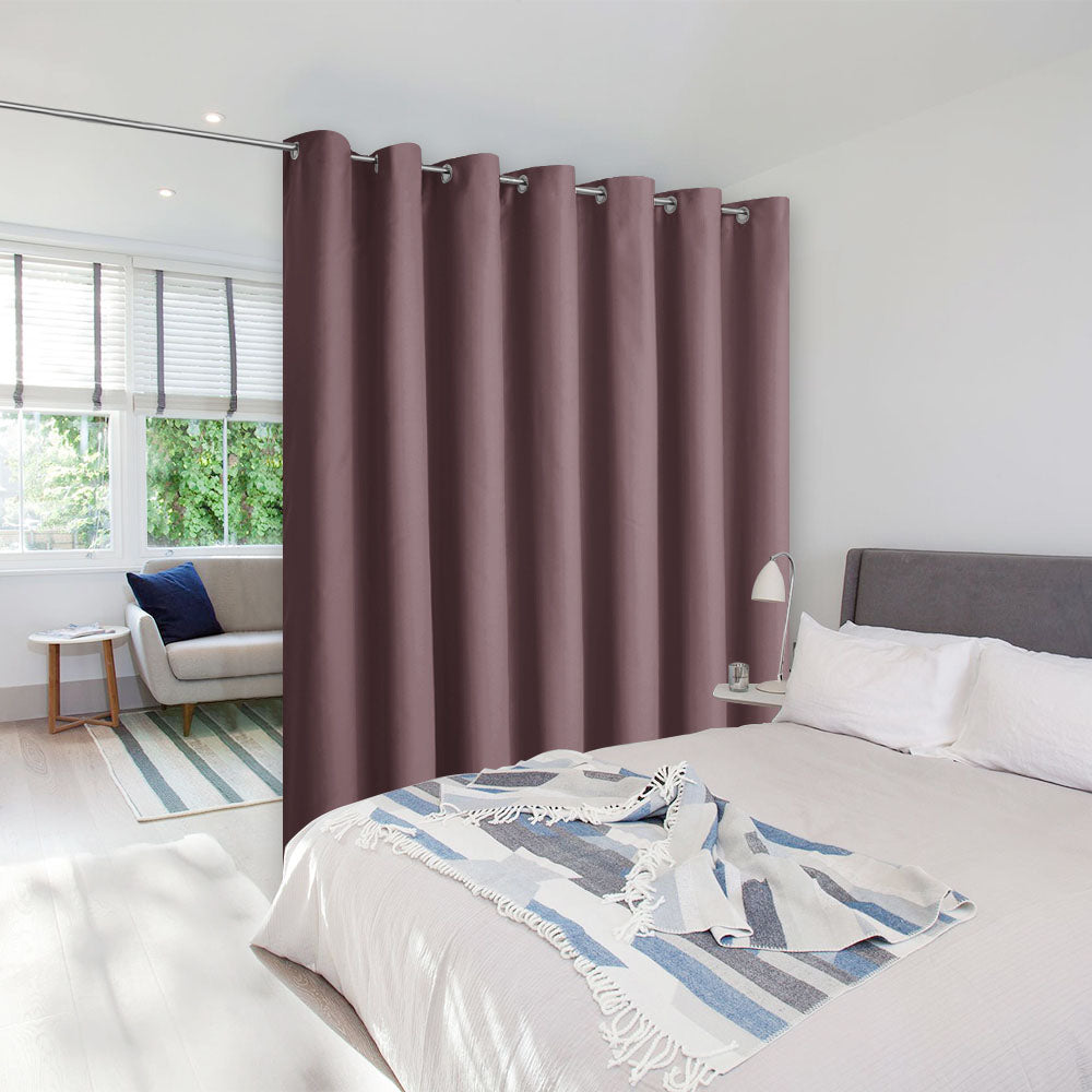 A mauve room divider curtain on a tension rod creates a private bedroom space in a bright, modern studio apartment.